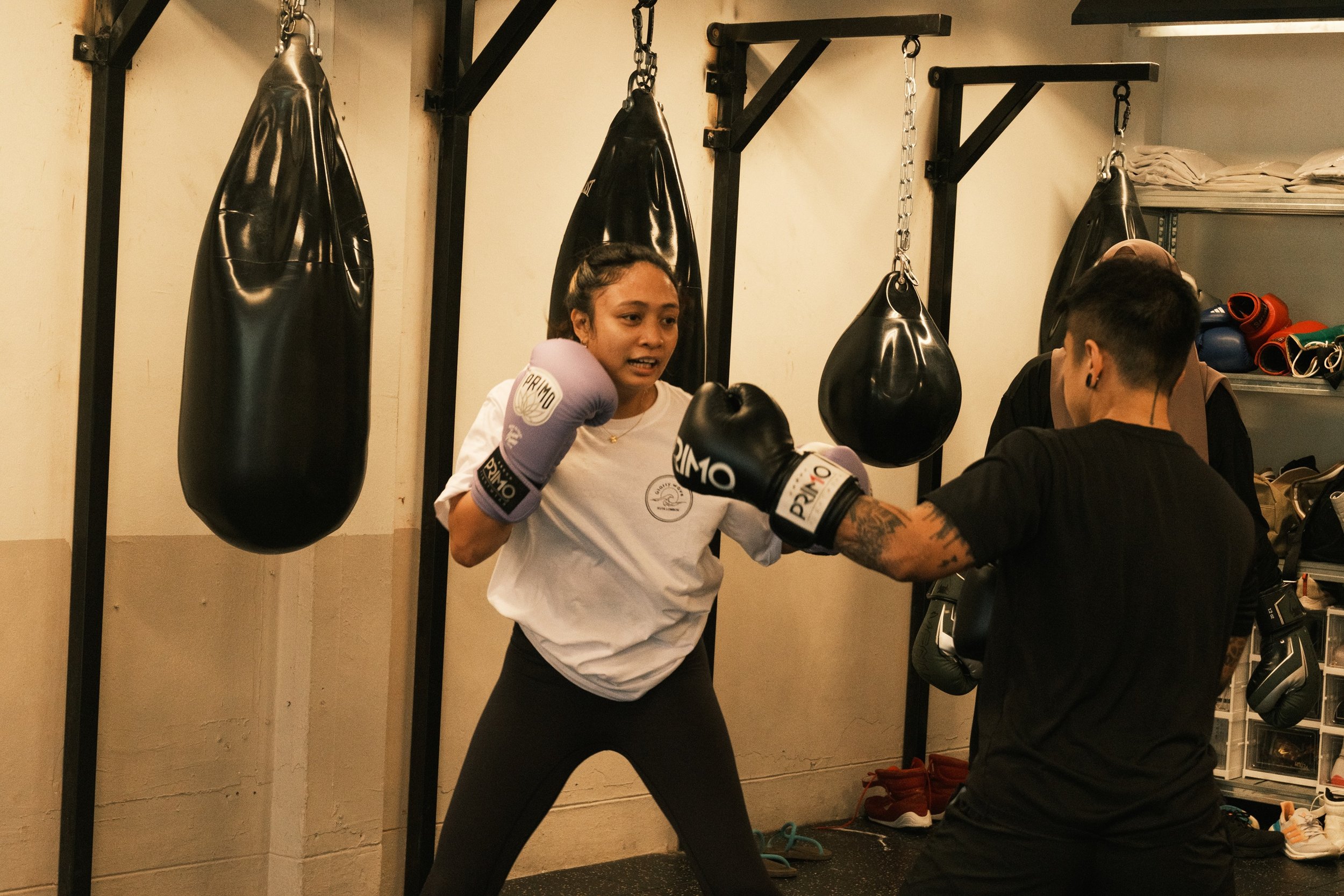Woman in lavender Primo boxing gloves throwing a punch during pad work with coach at a female boxing class in Singapore