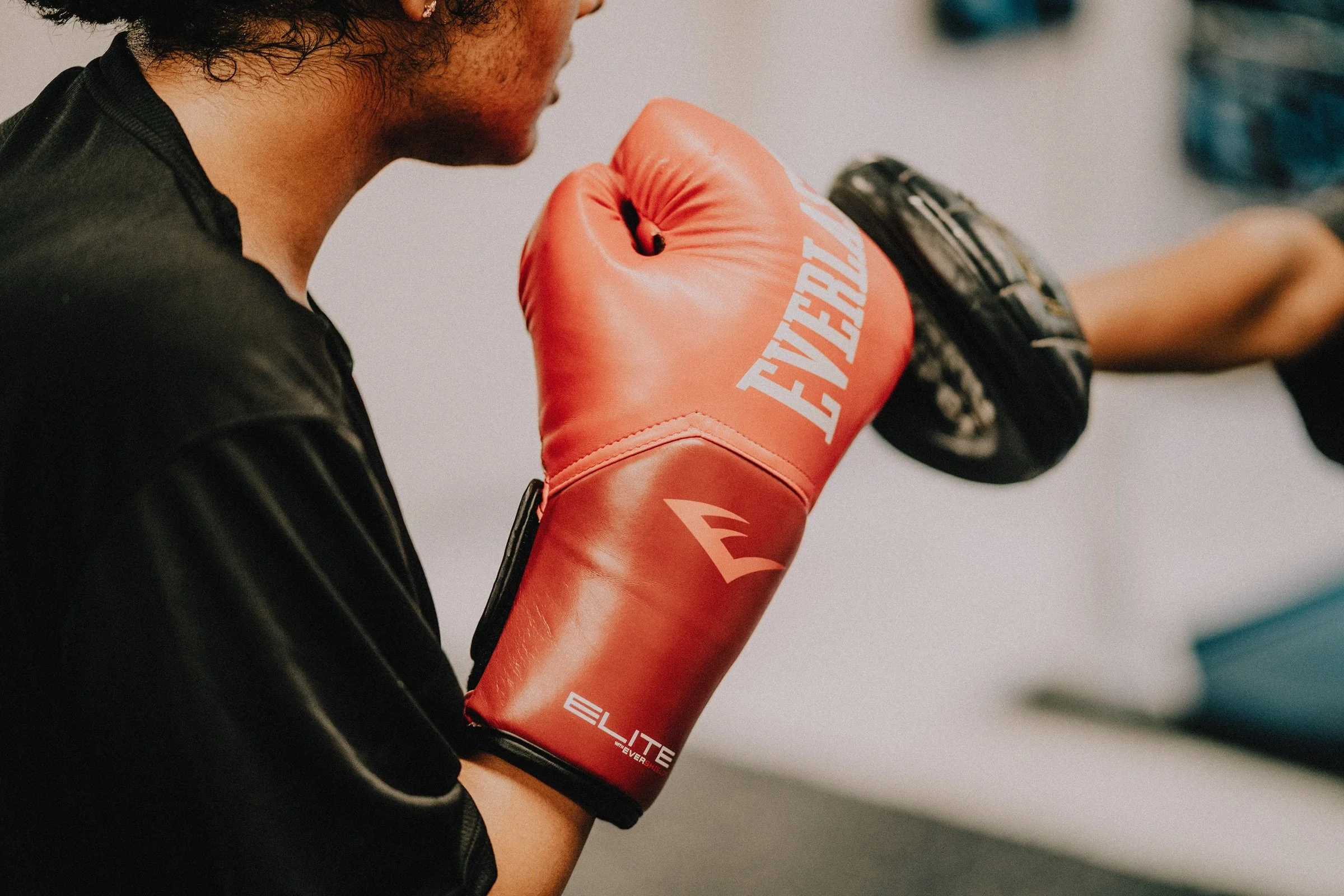 Close-up of a boxer in a red Everlast glove punching a focus mitt held by a coach during pad work at Sweat Science Studio.
