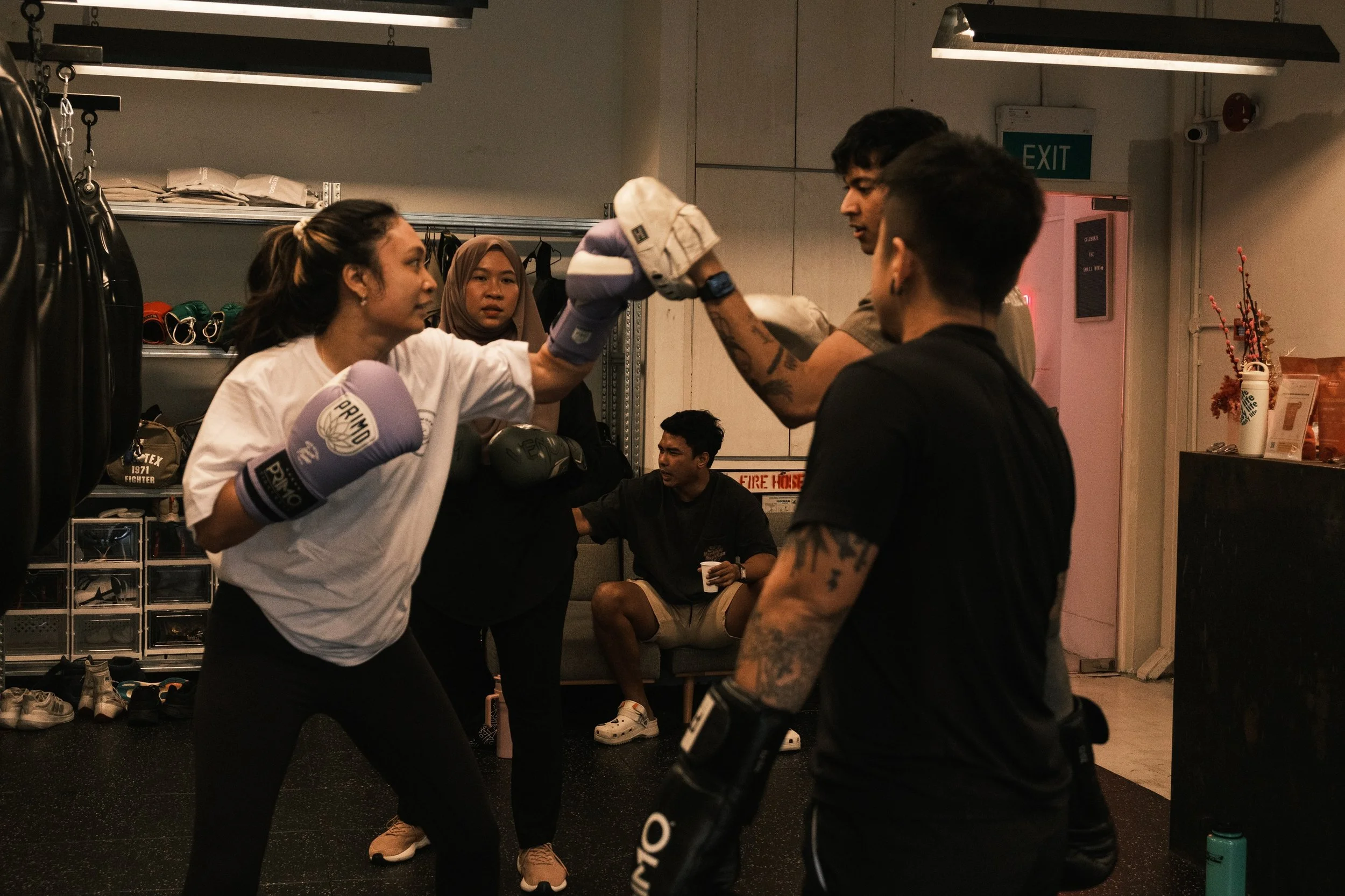 Female boxer in purple Primo gloves doing padwork with a coach at Sweat Science Studio, a boutique boxing gym in Singapore