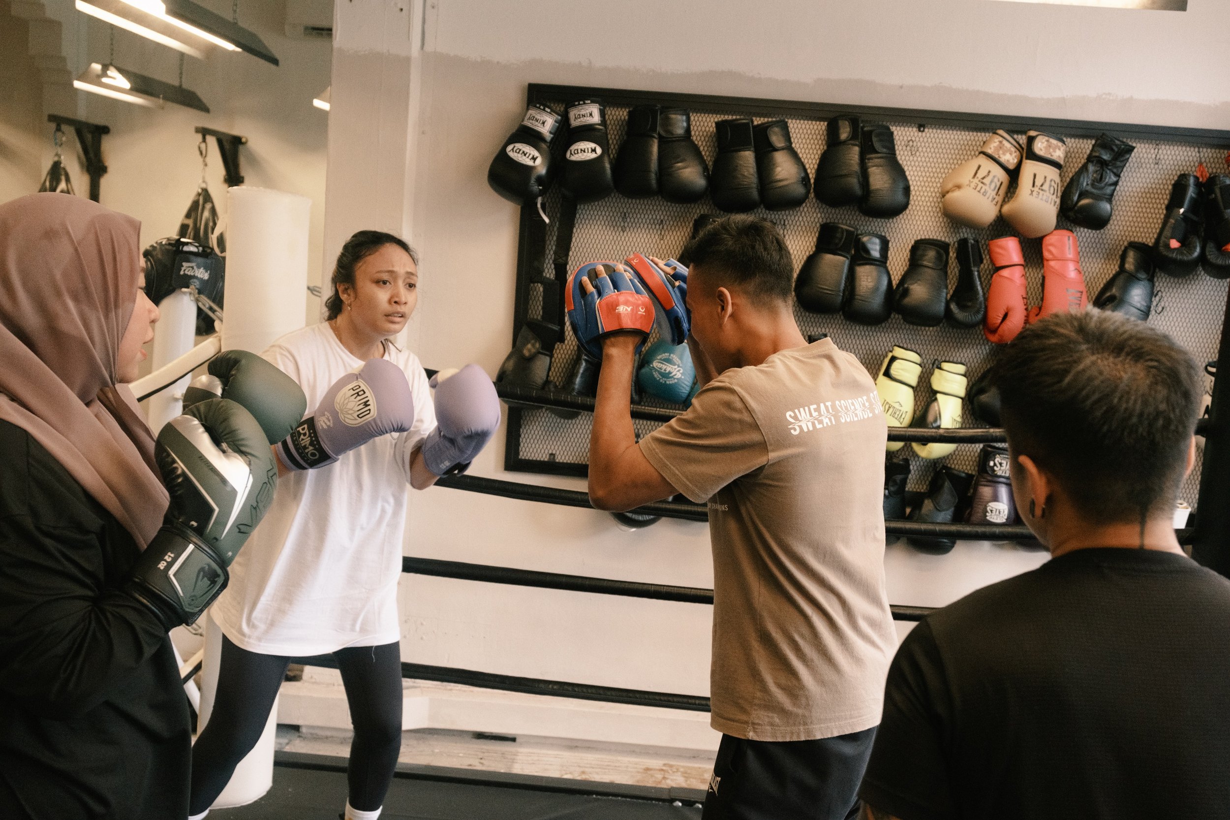 Boxing coach holding focus mitts for pad work training at Sweat Science Studio boxing gym in Singapore