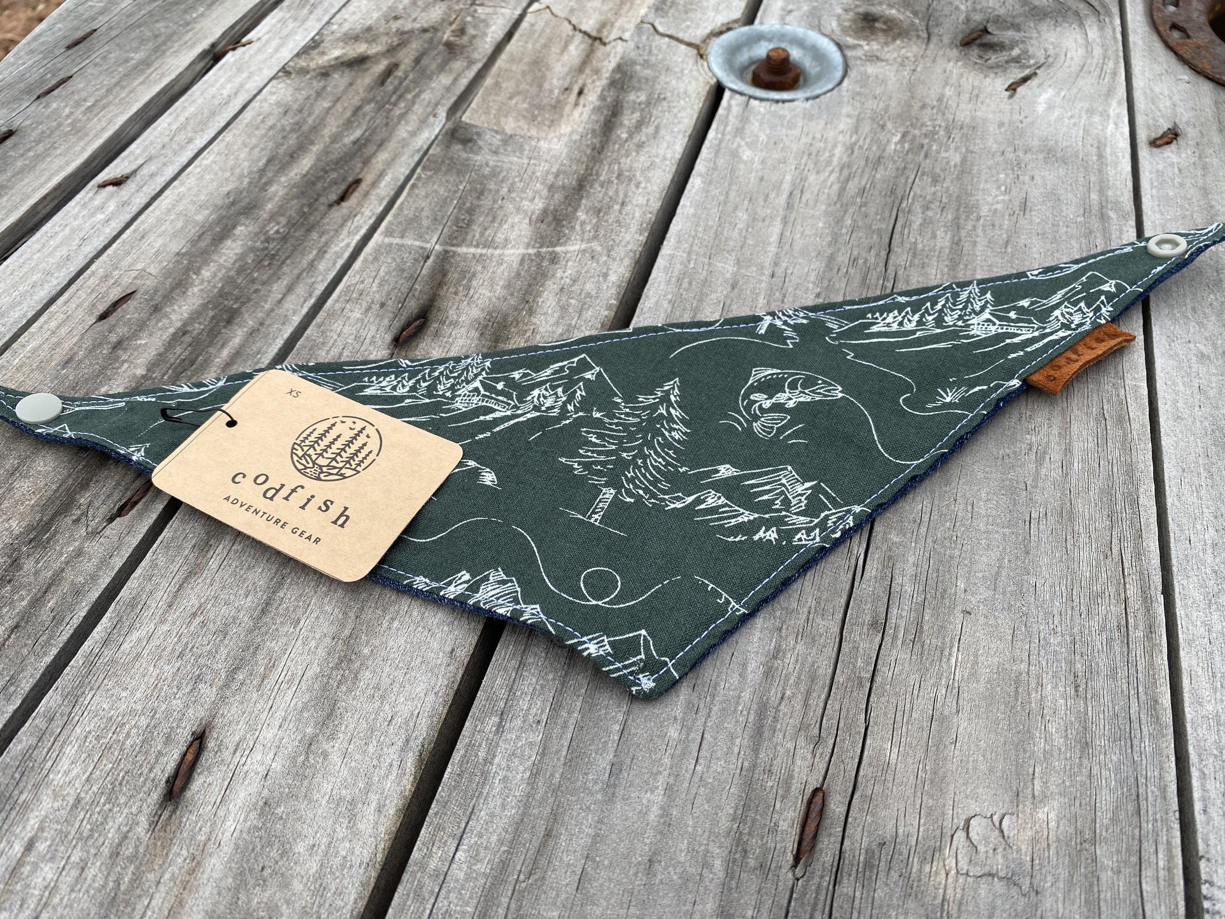 white line drawing of fish caught on the line, cabin in the mountains, forest trees on dark green background dog bandana