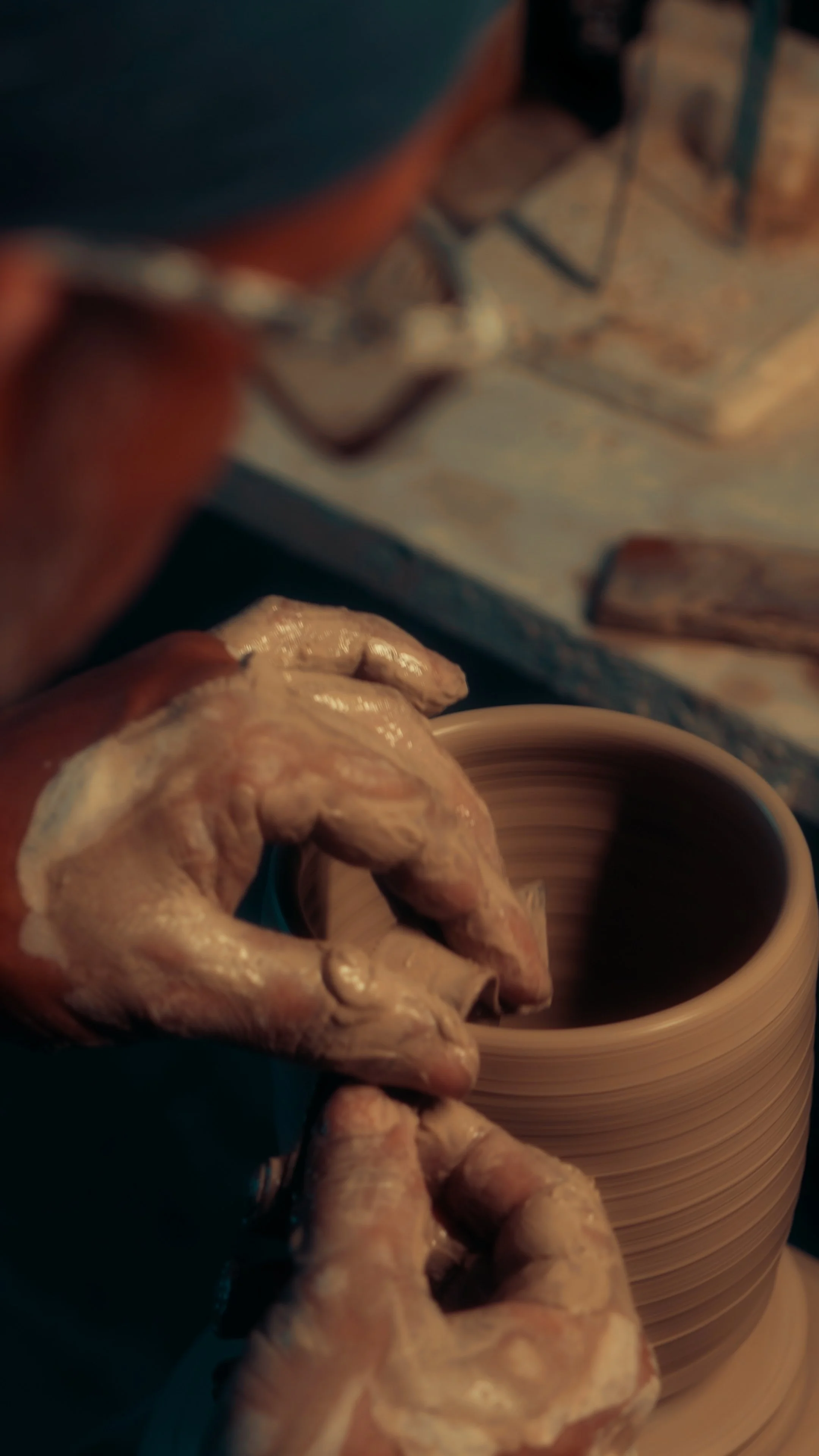 Close-up of a person shaping clay on a pottery wheel, with their hands covered in wet clay.