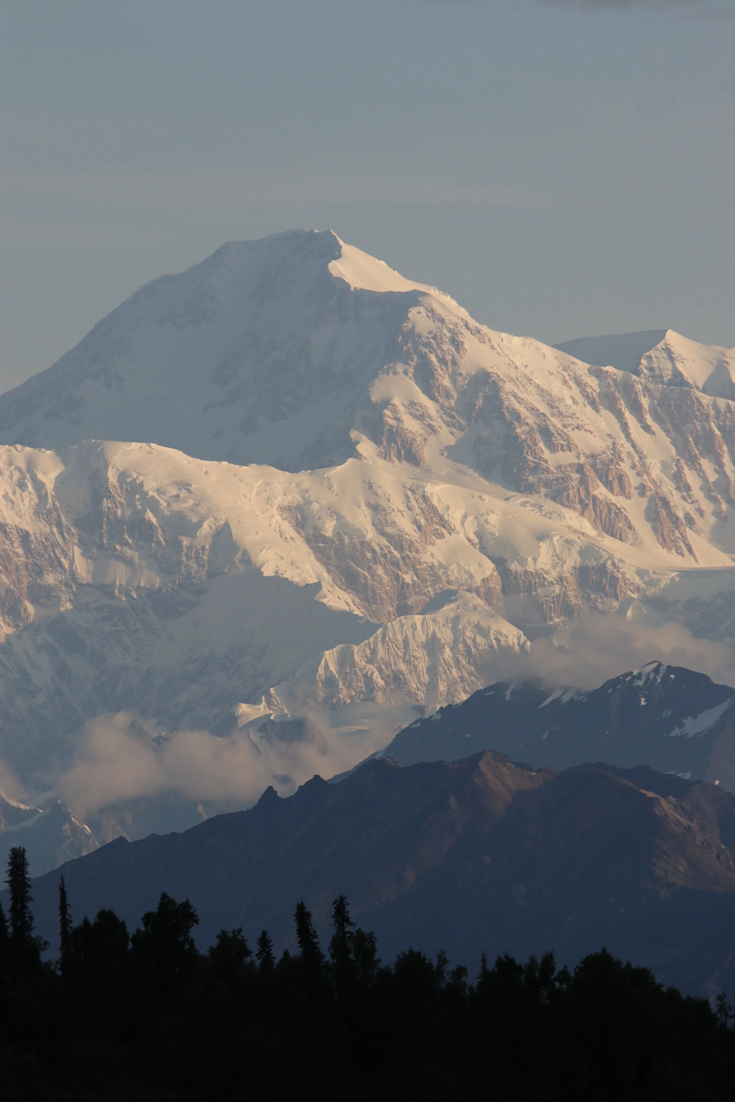 Snow-covered mountain peak with rugged lower terrain and scattered clouds.