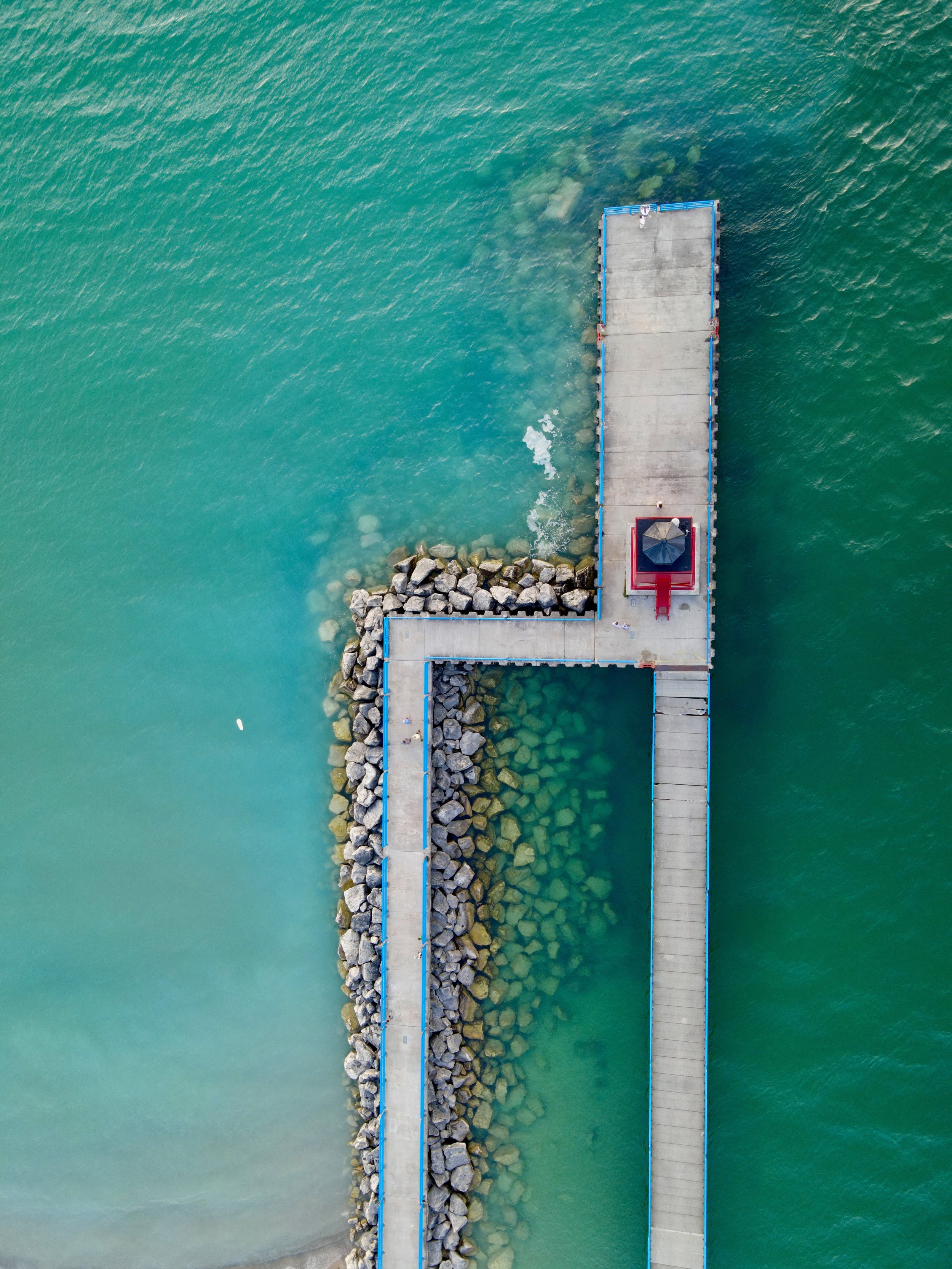 Aerial view of a pier with rocks along its sides extending into turquoise water.