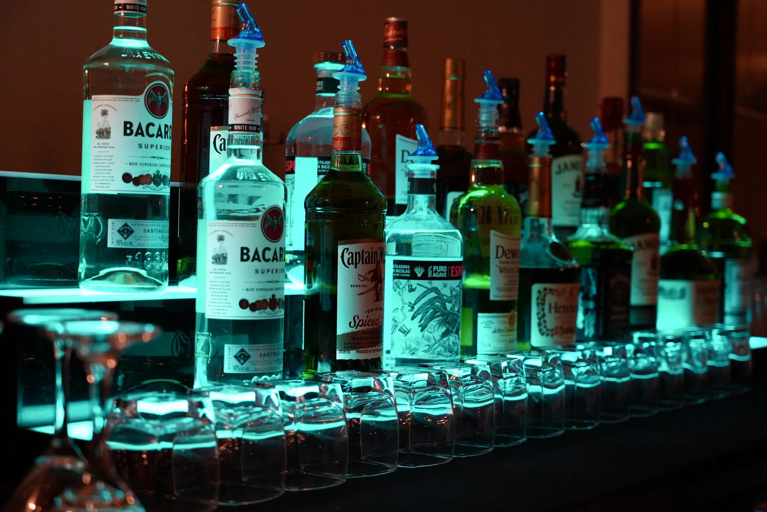 Bar counter with assorted liquor bottles and upside-down glasses, illuminated with blue lighting.