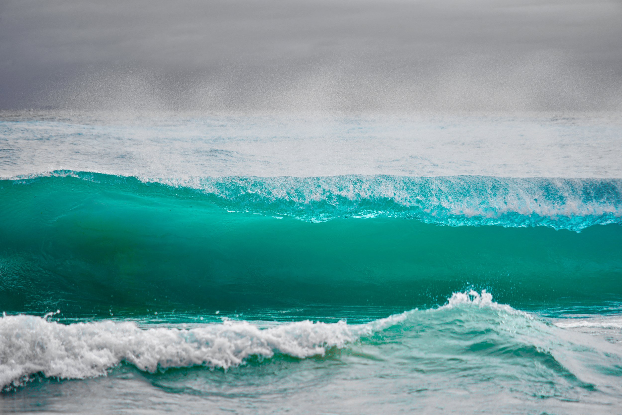 Ocean wave breaking in turquoise water under a cloudy sky.