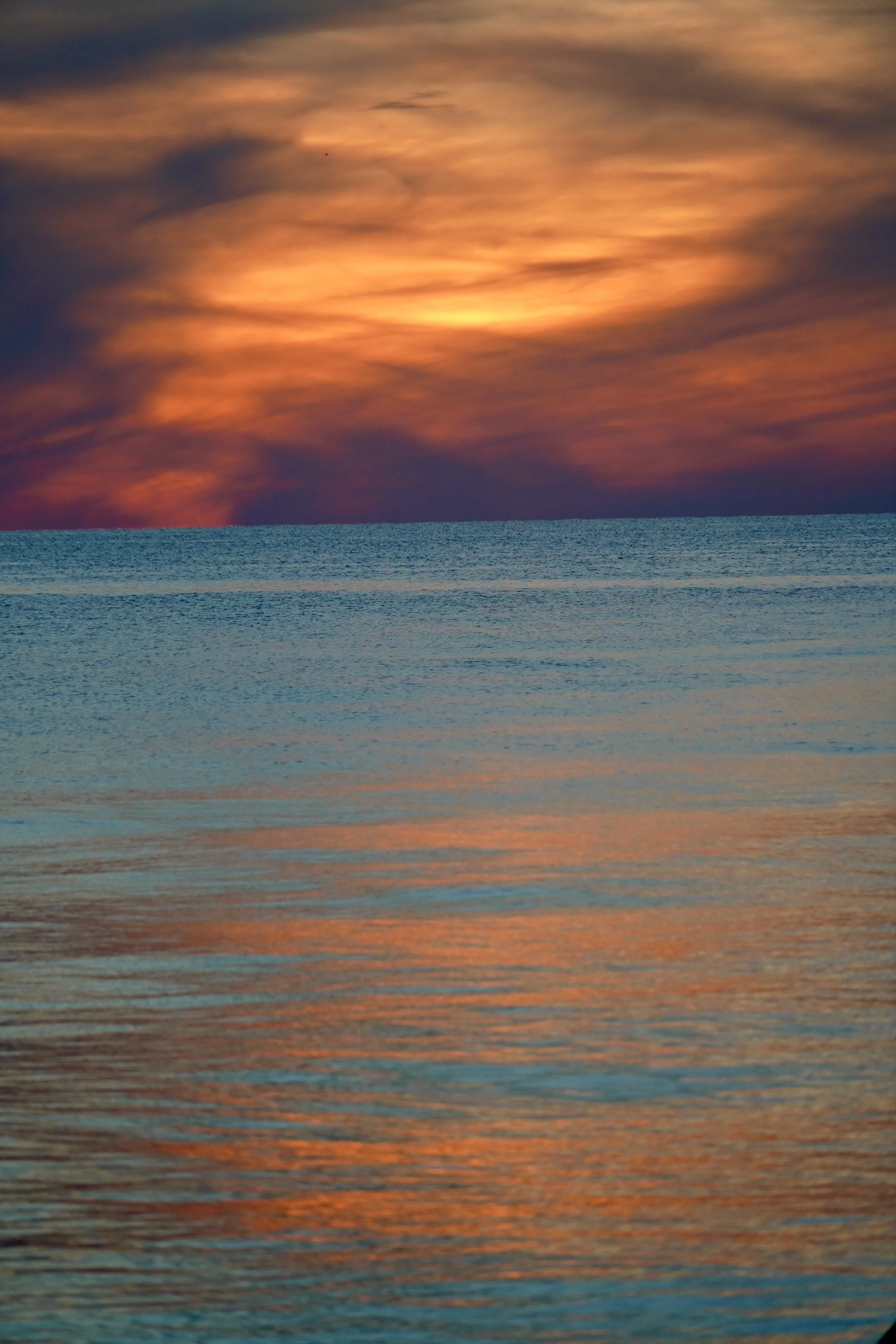 Sunset over the ocean with vibrant orange and pink hues in the sky and water reflections.