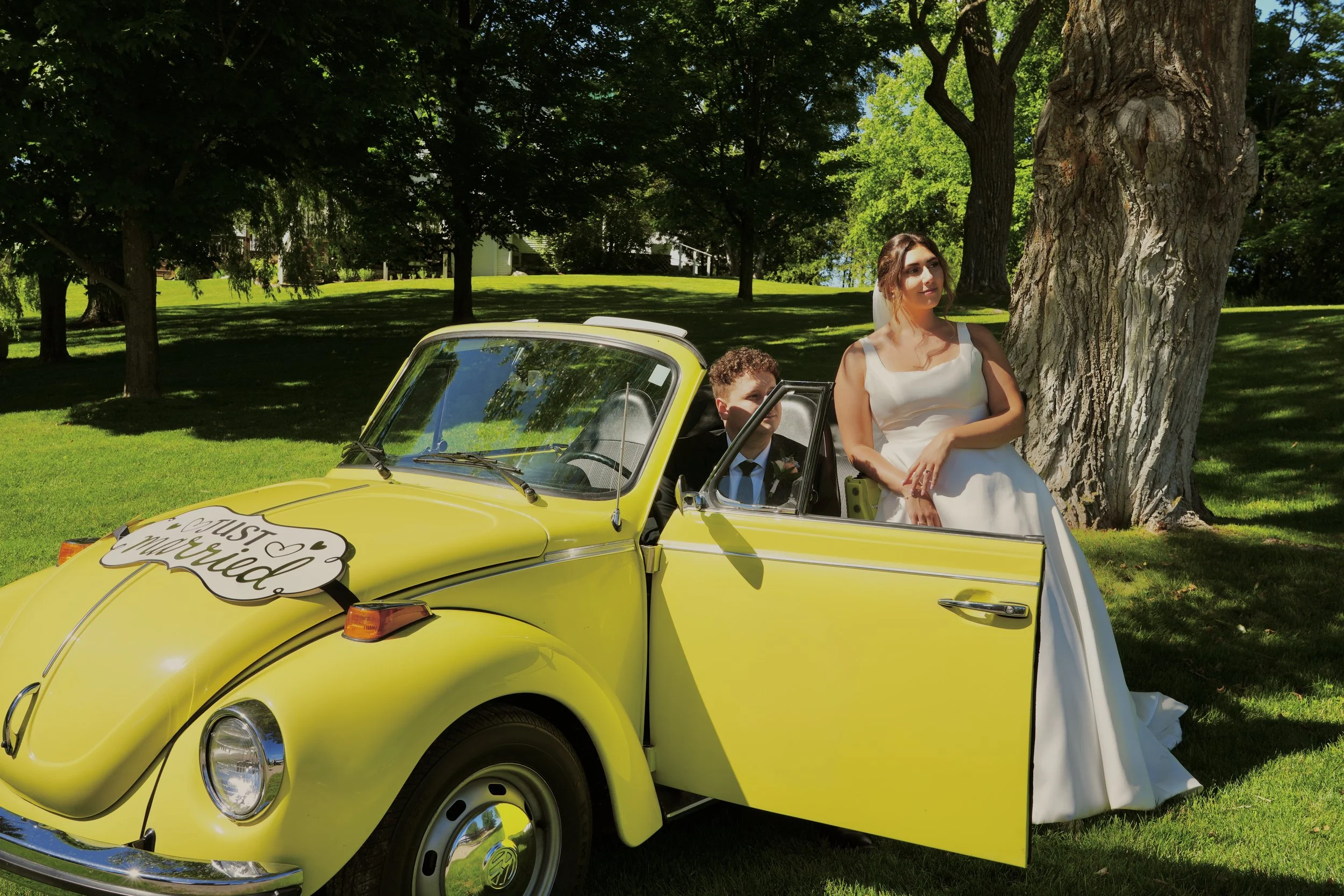 Bride and groom with a yellow Volkswagen Beetle decorated with a "Just Married" sign in a park