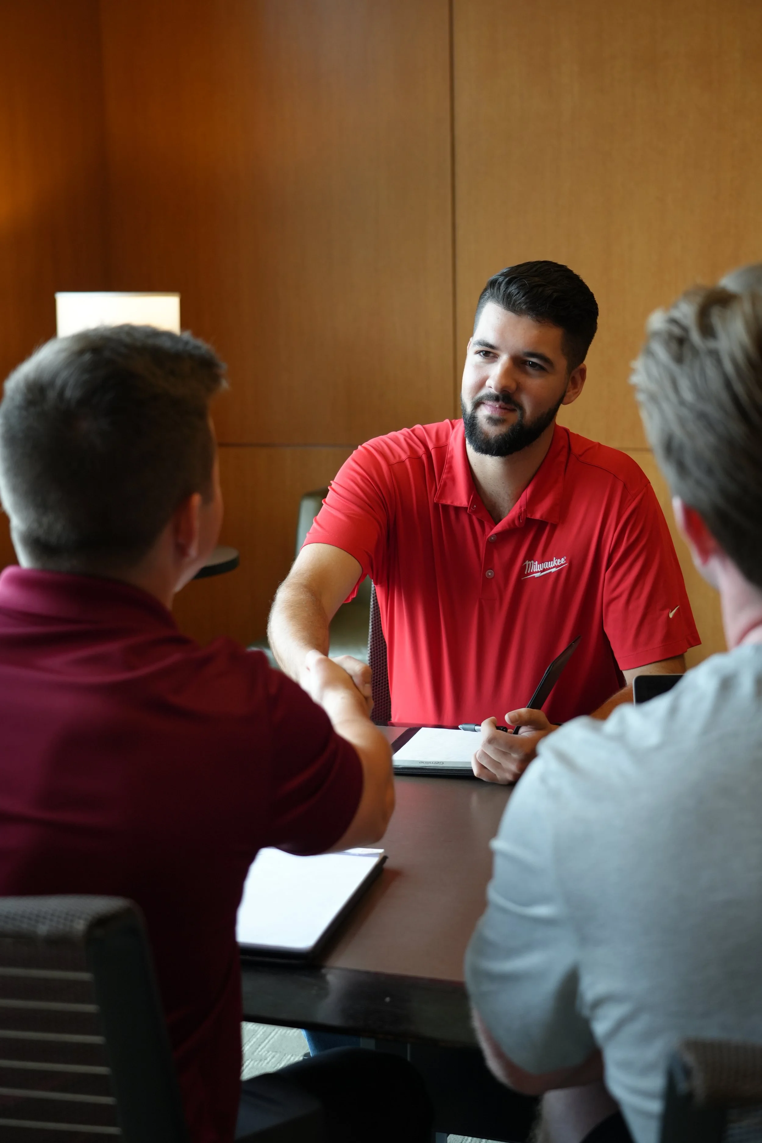 Group meeting with three men, one shaking hands, in a formal setting.