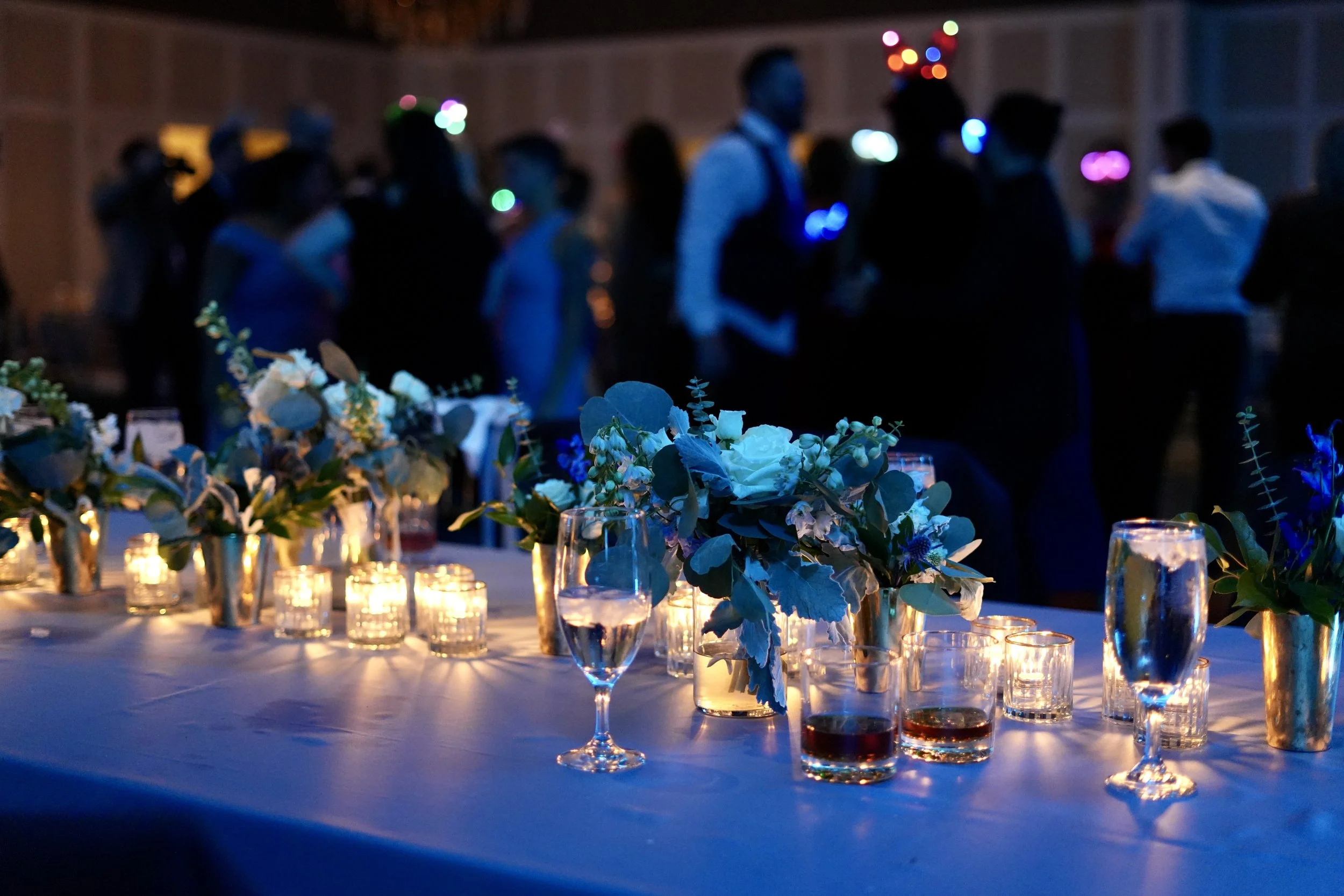 Table with candles and floral arrangements at a dimly lit event.