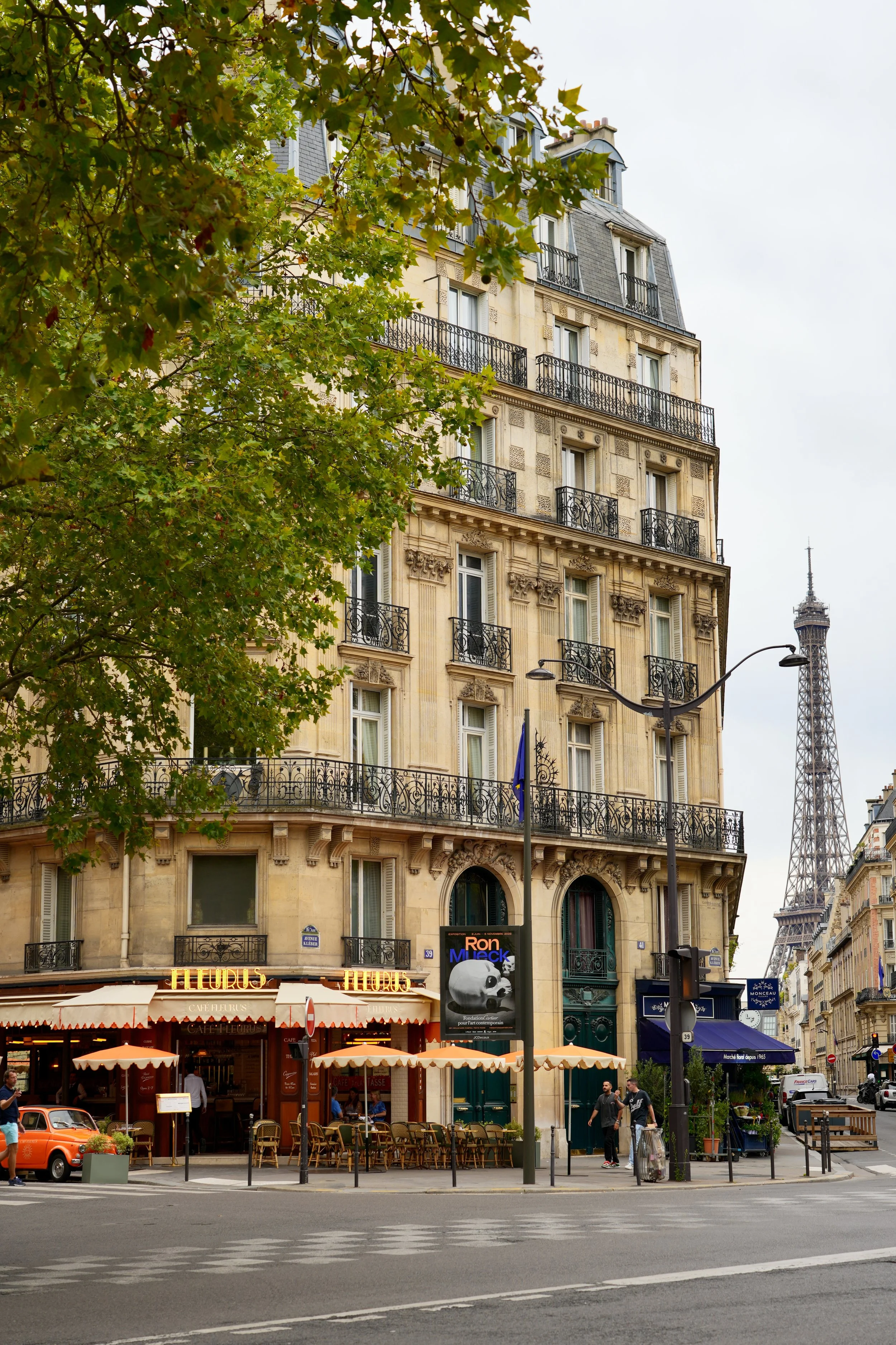 Parisian street scene with historic building, outdoor café, and Eiffel Tower in the background.