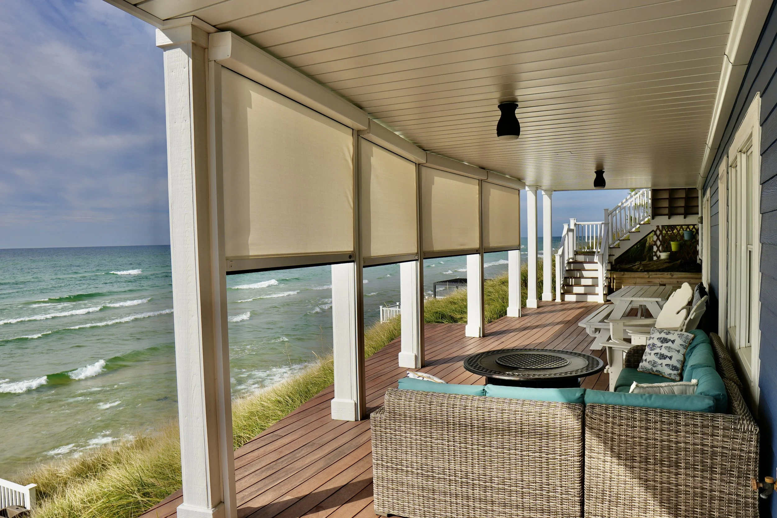 Beachfront porch with wicker furniture, white pillars, retractable blinds, and ocean view.
