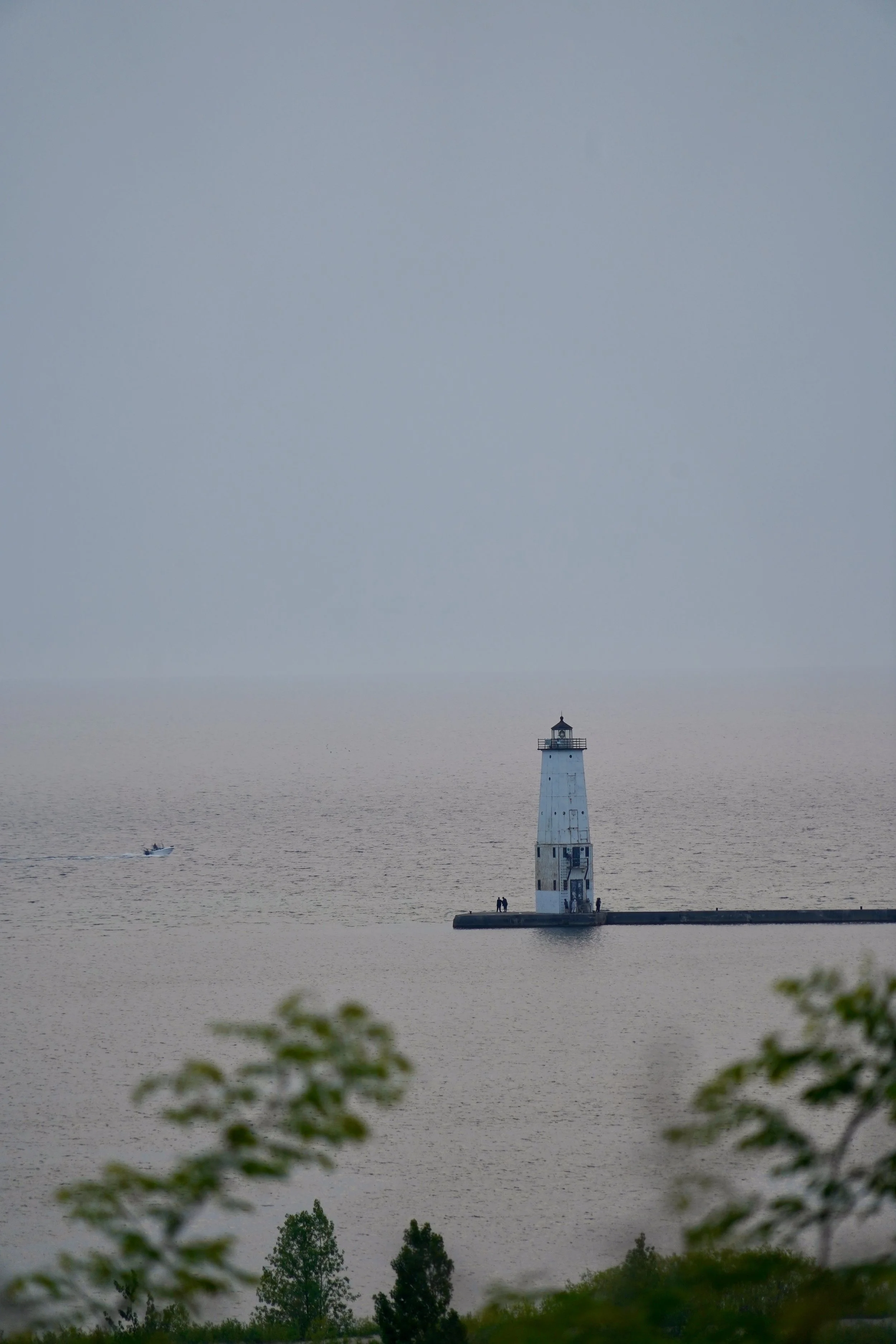 Lighthouse on a pier surrounded by water, with a small boat nearby and trees in the foreground.