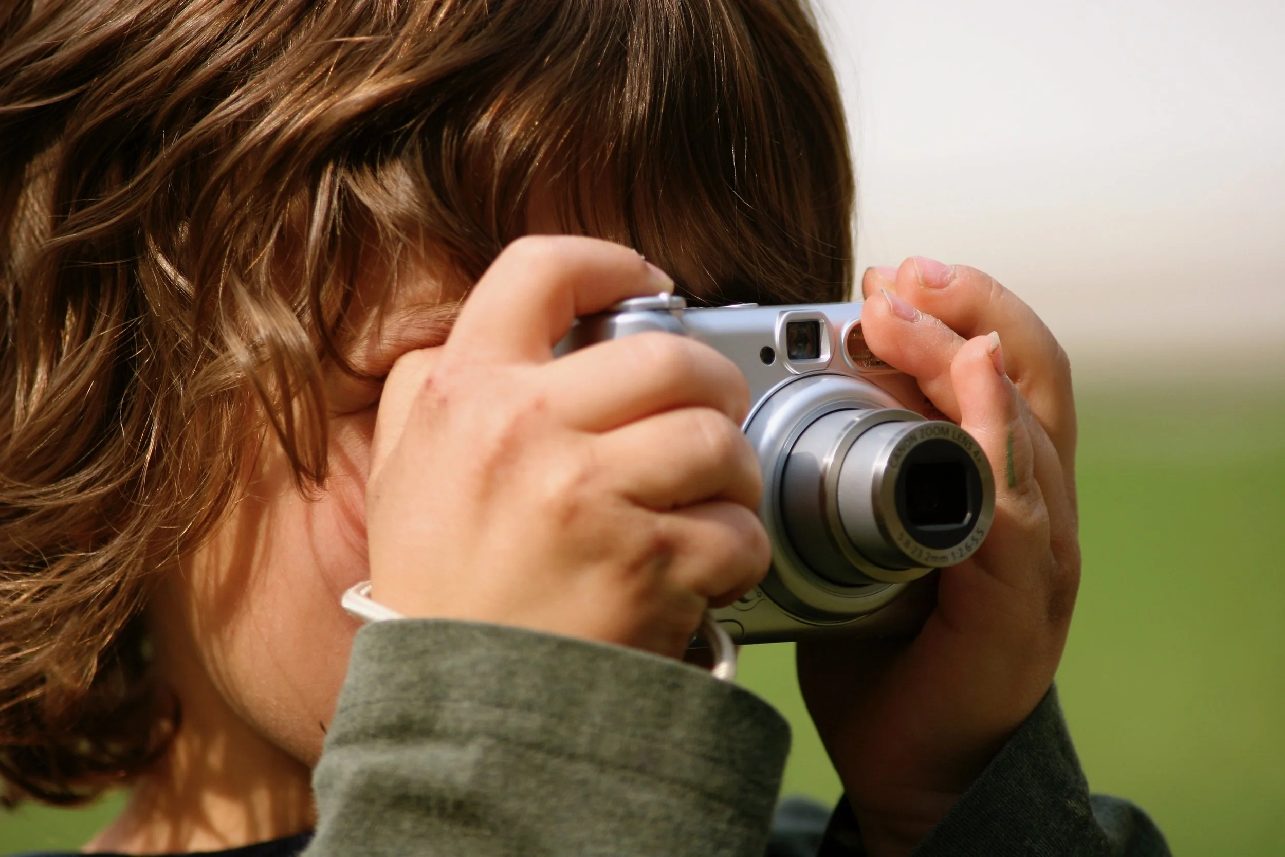 Child holding a digital camera and taking a photo, focusing through the viewfinder.
