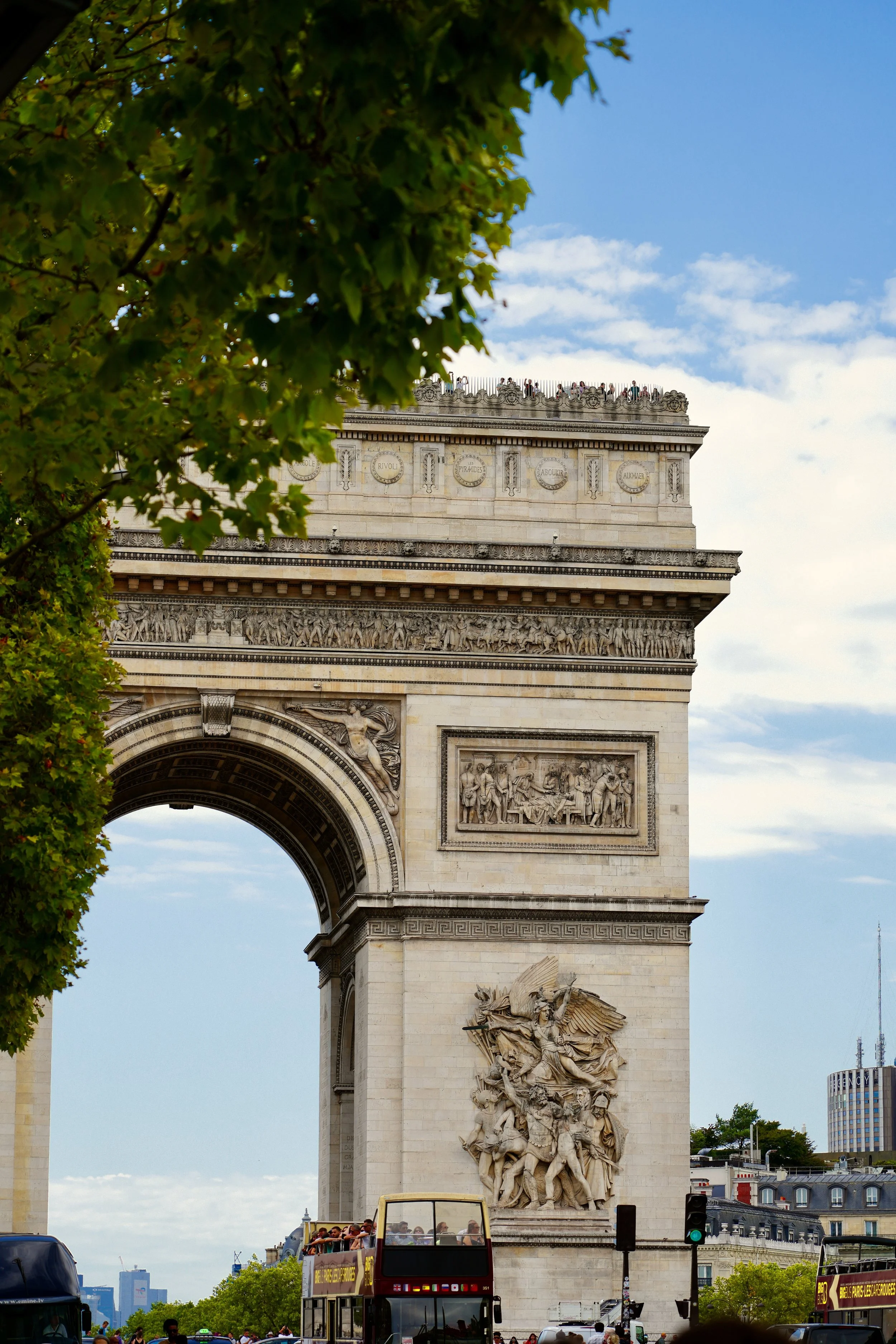 Arc de Triomphe in Paris with a tour bus, trees, and a clear sky.