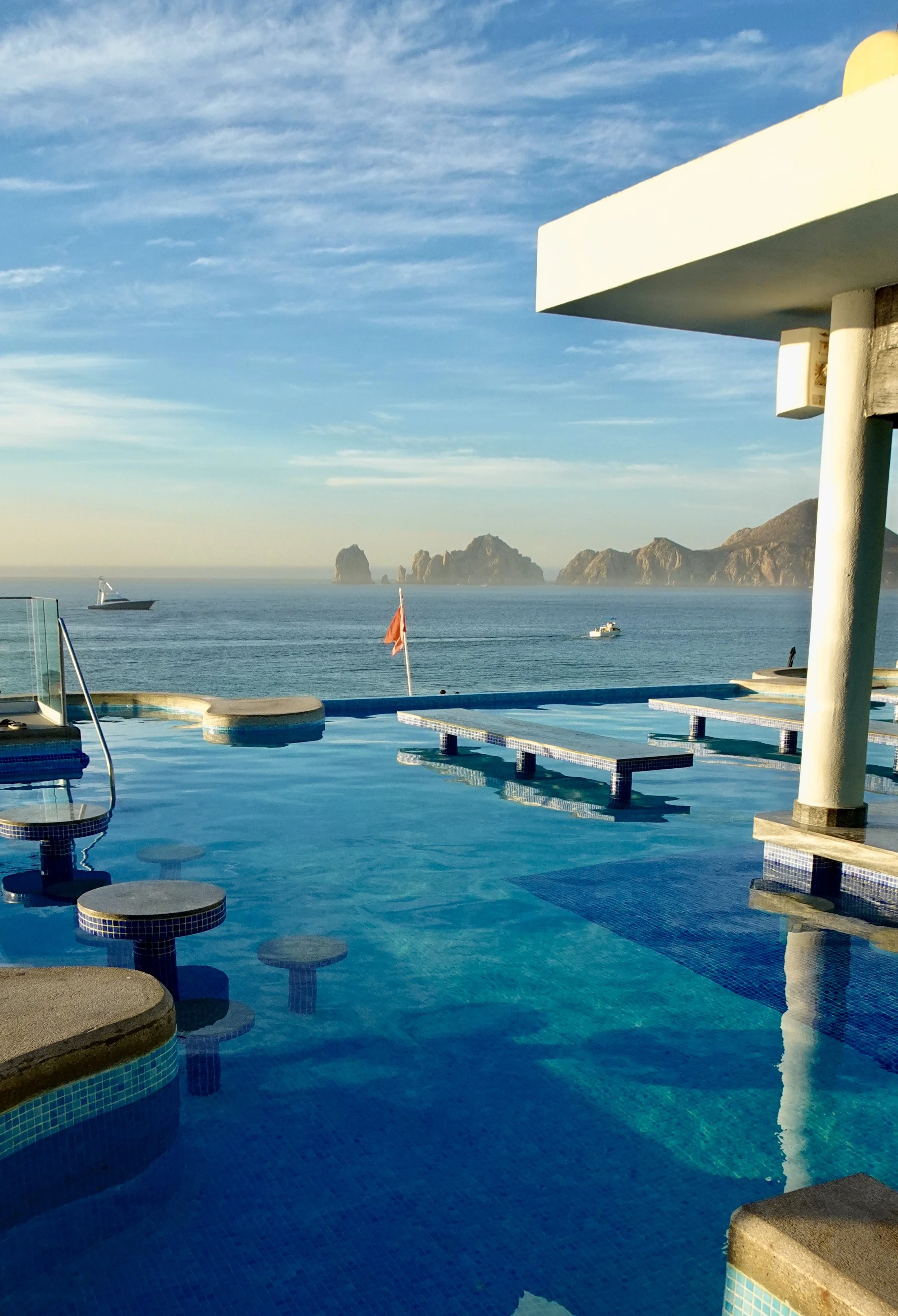 Infinity pool with ocean and rocky landscape in background, under clear blue sky.