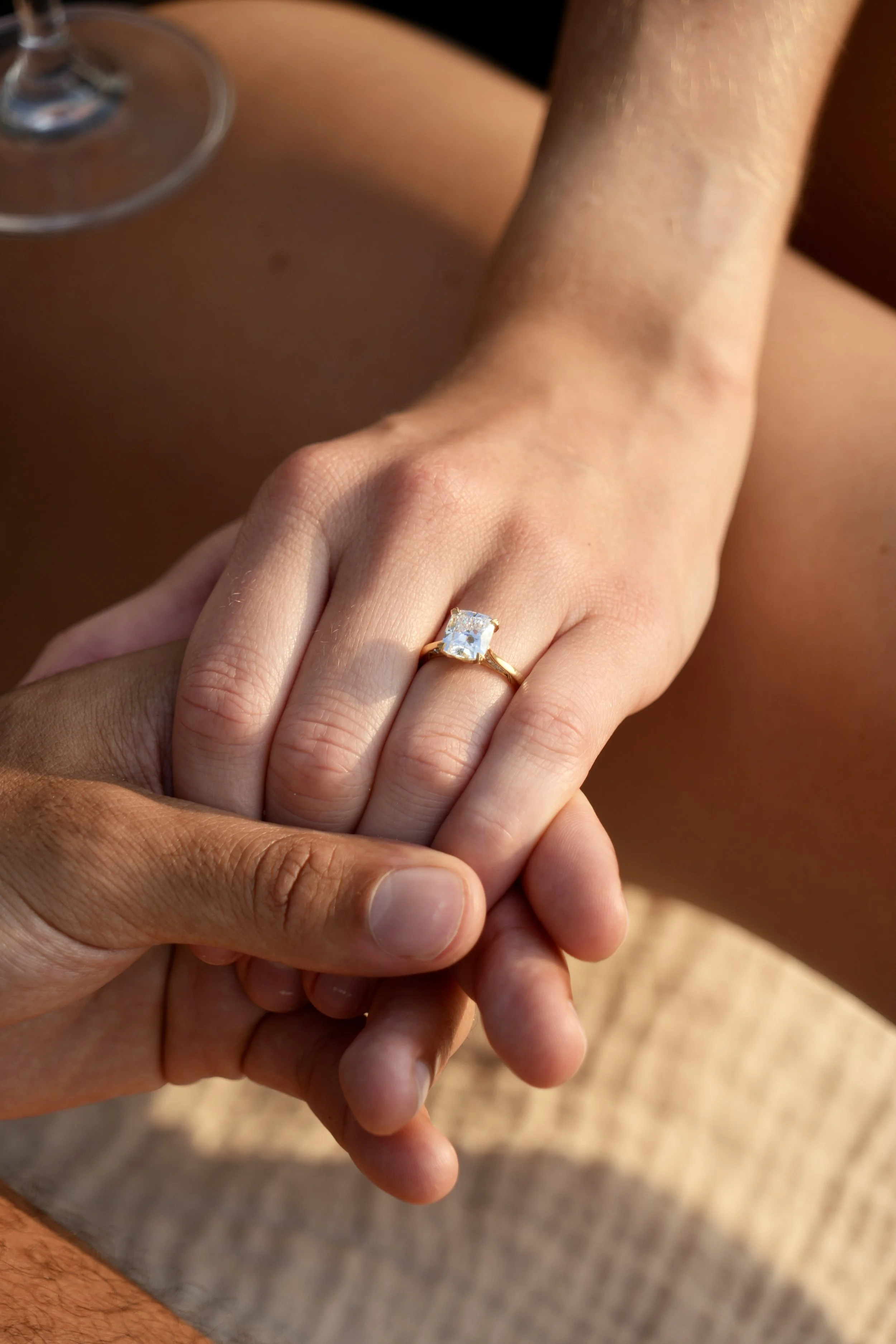 Close-up of two hands holding; one is wearing a gold ring with a large square diamond, showing engagement.