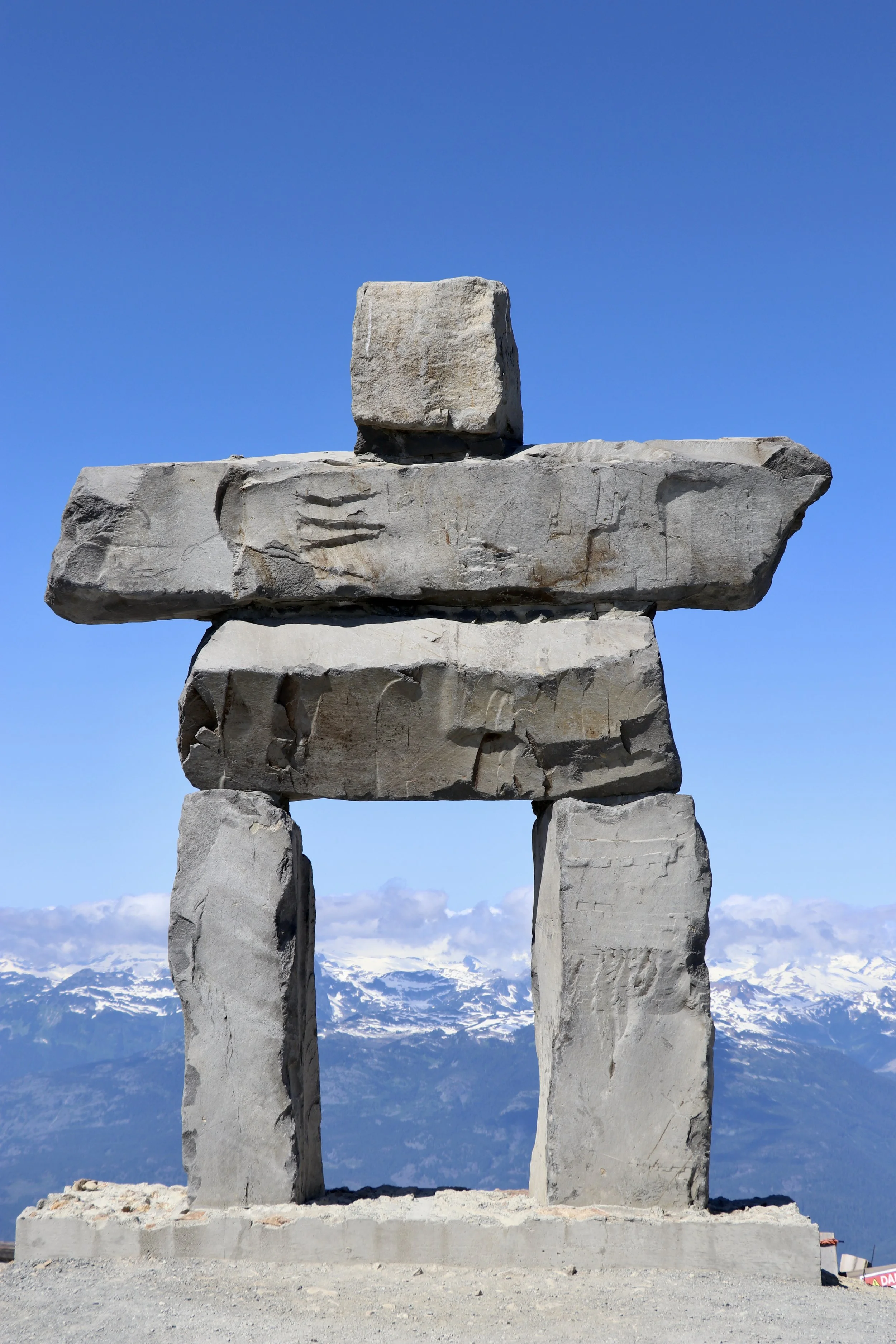 Stone inukshuk with snowy mountain background and clear blue sky