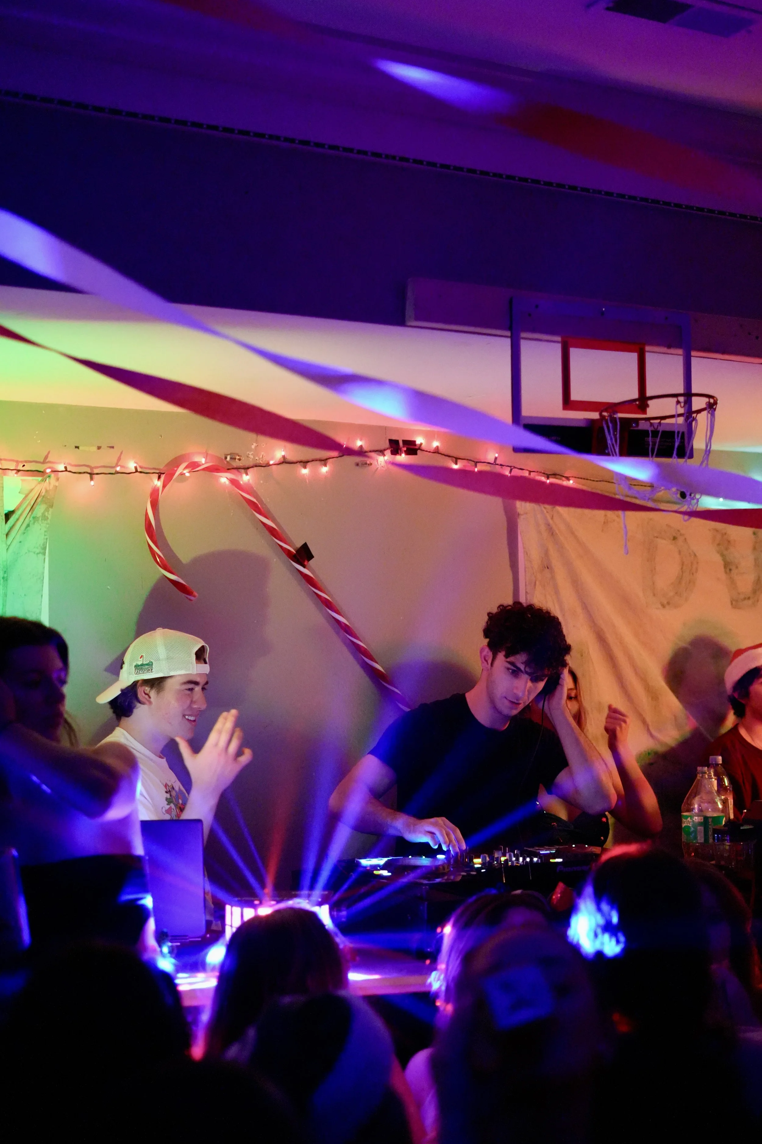 DJ performing at a party with colorful lights and decorations, including a basketball hoop and Christmas-themed ornaments.