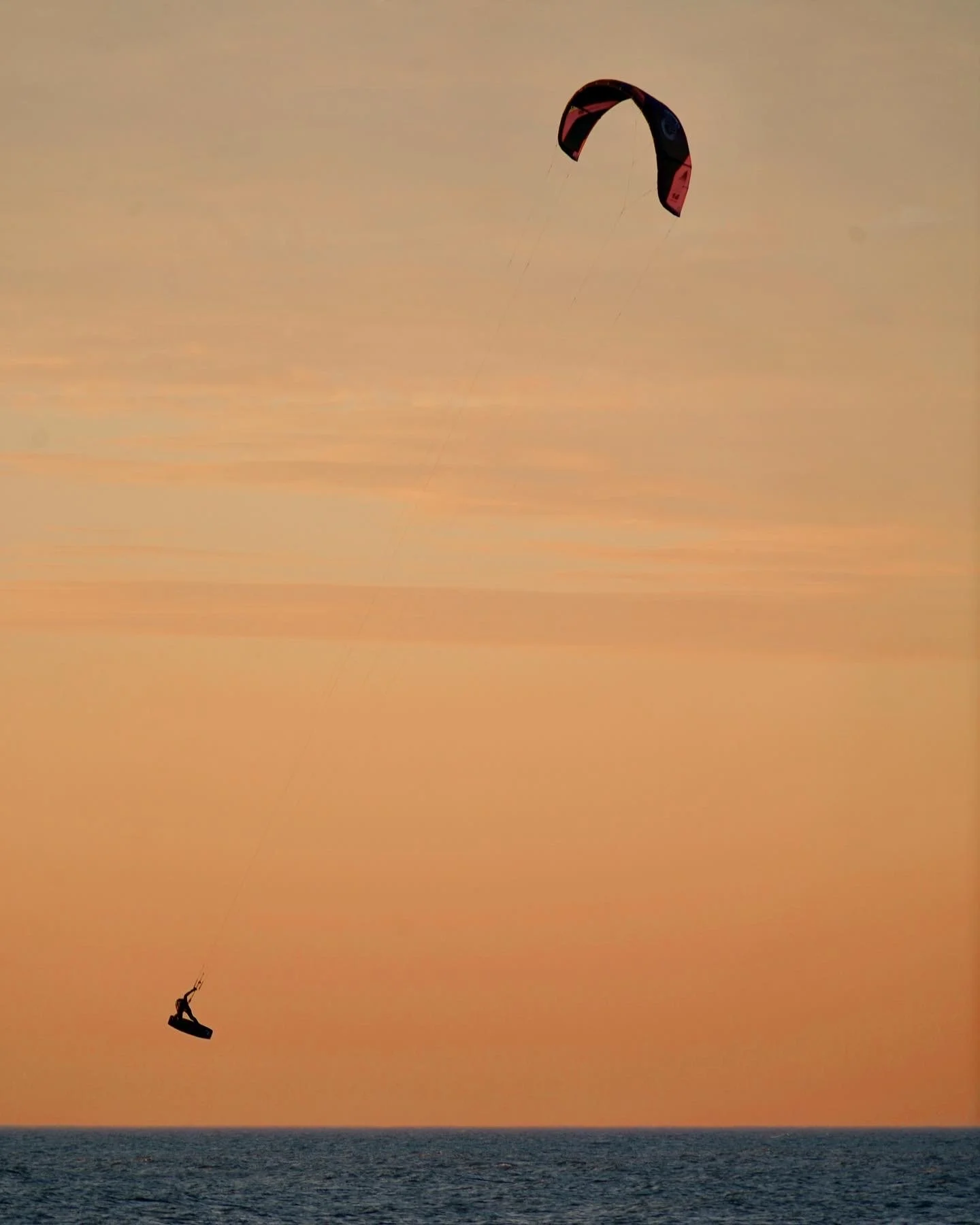 Kitesurfer jumping over the ocean at sunset with a kite in the sky.