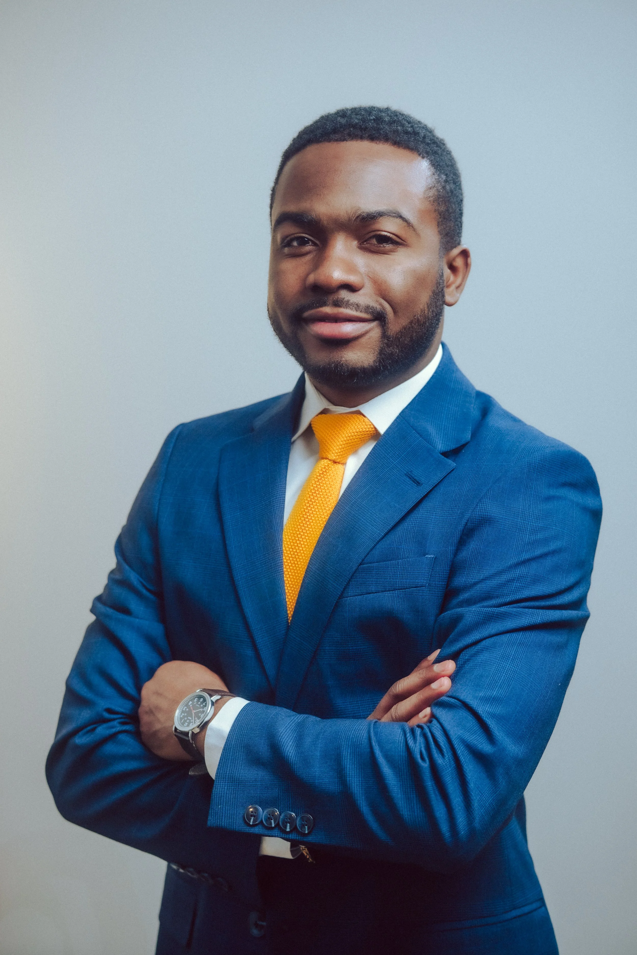 A man in a blue suit and yellow tie smiling, standing indoors.