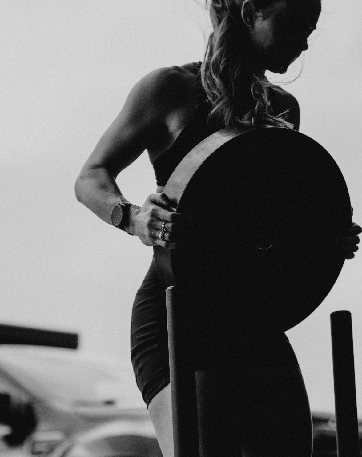 A woman in workout attire performing a pull-up in a gym with a power rack and open garage door.