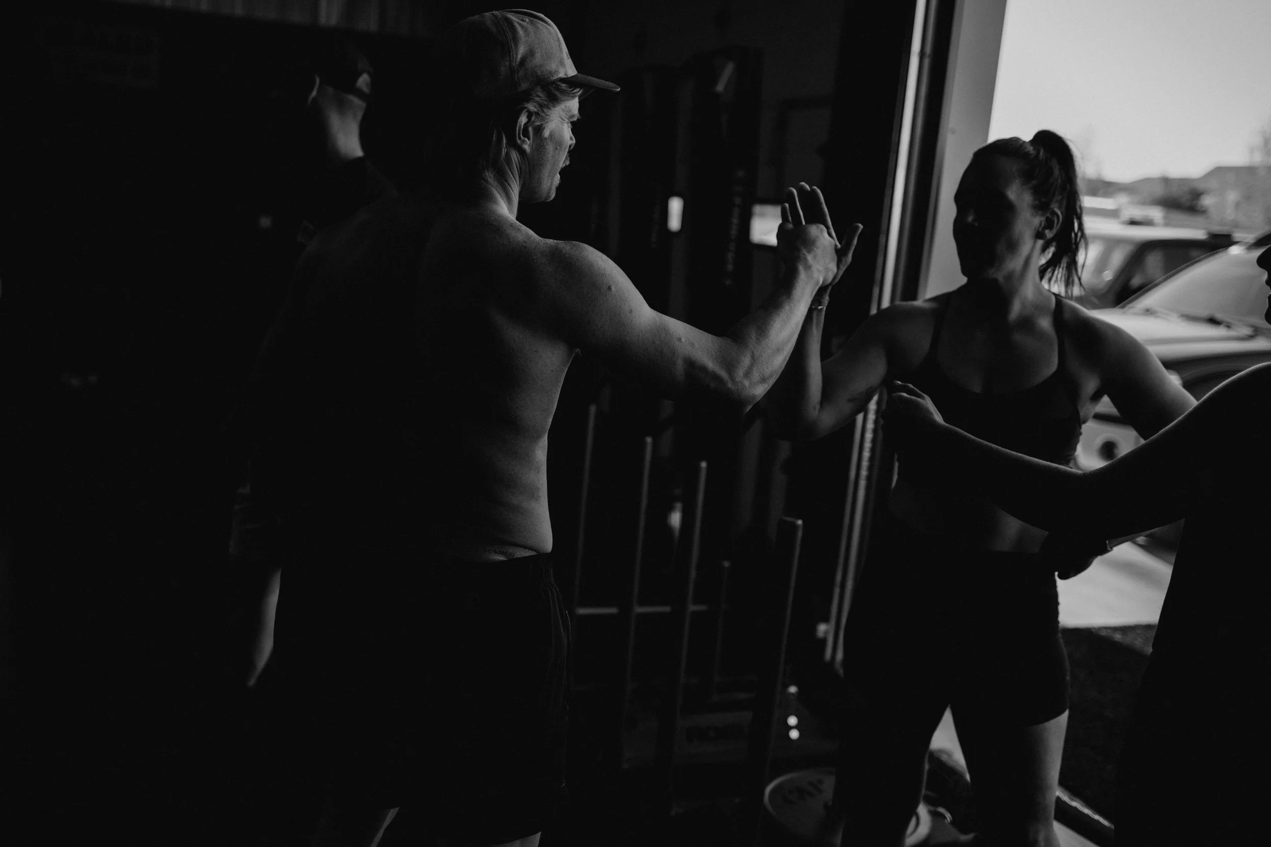 A woman in workout attire performing a pull-up in a gym with a power rack and open garage door.
