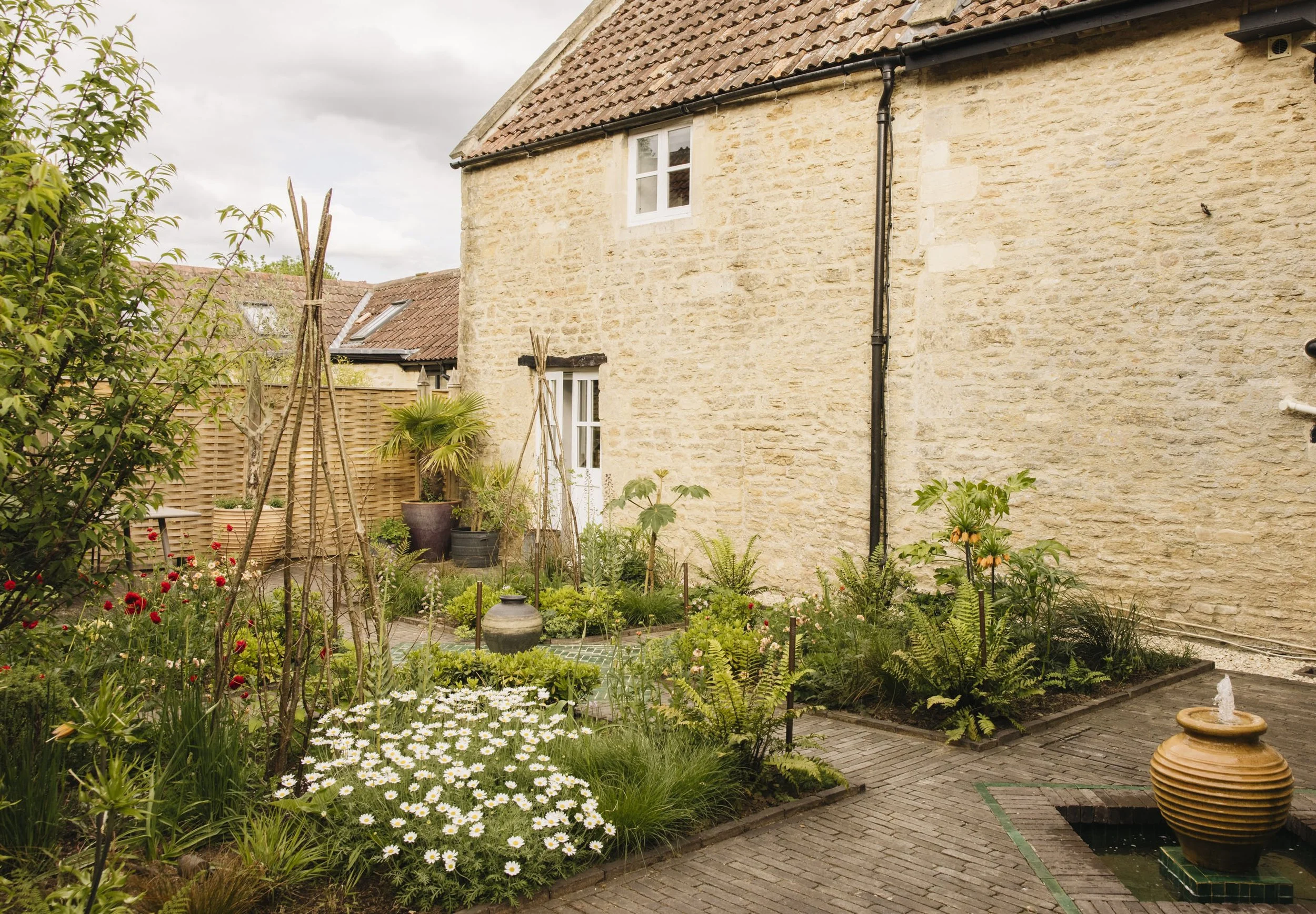 Garden with colourful flowers, large potted plants, a water fountain, brick paved walkway. Photo taken by Eva Nemeth Garden Photographer