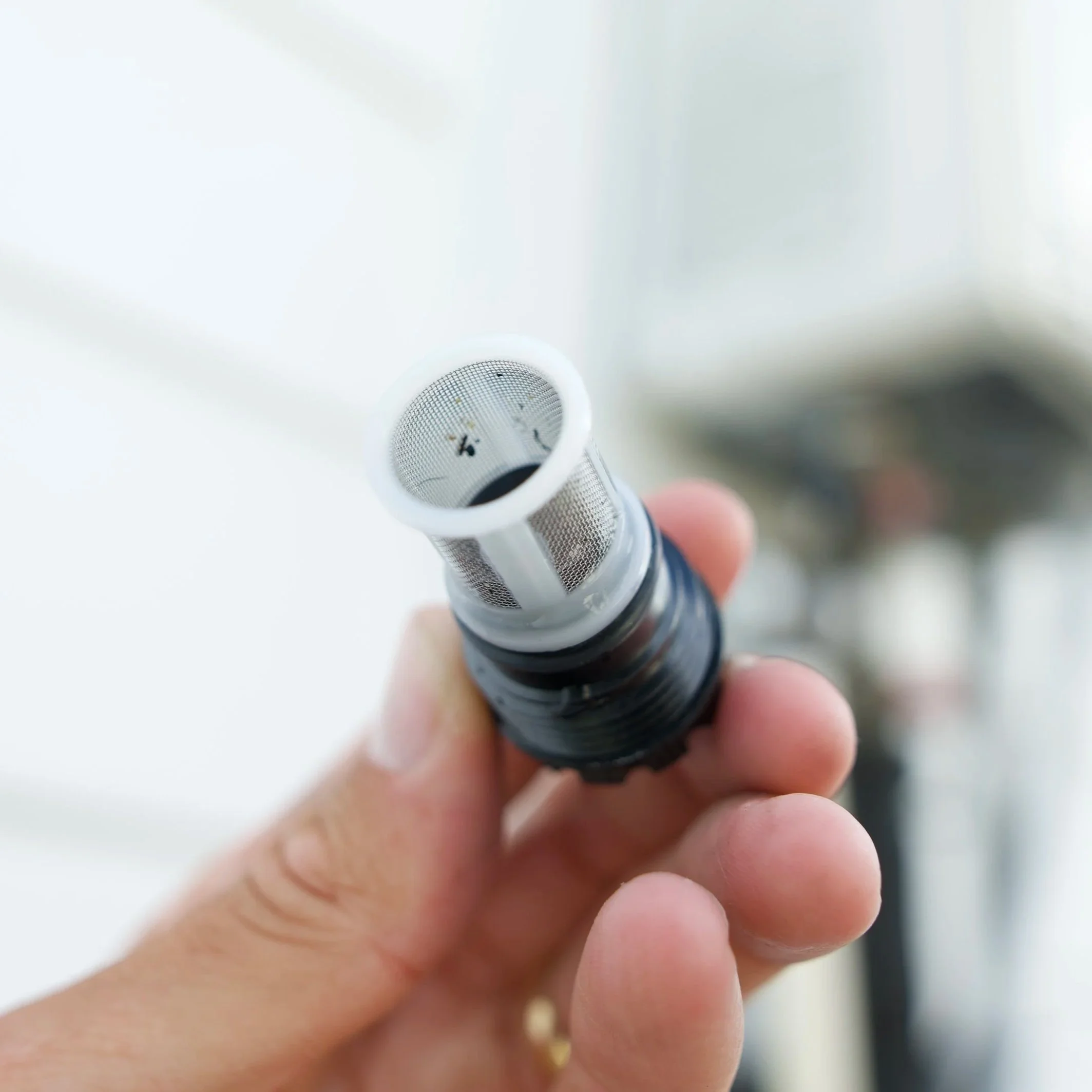 Close-up of a person holding a small flashlight with a metal mesh lens, with a blurred white background.