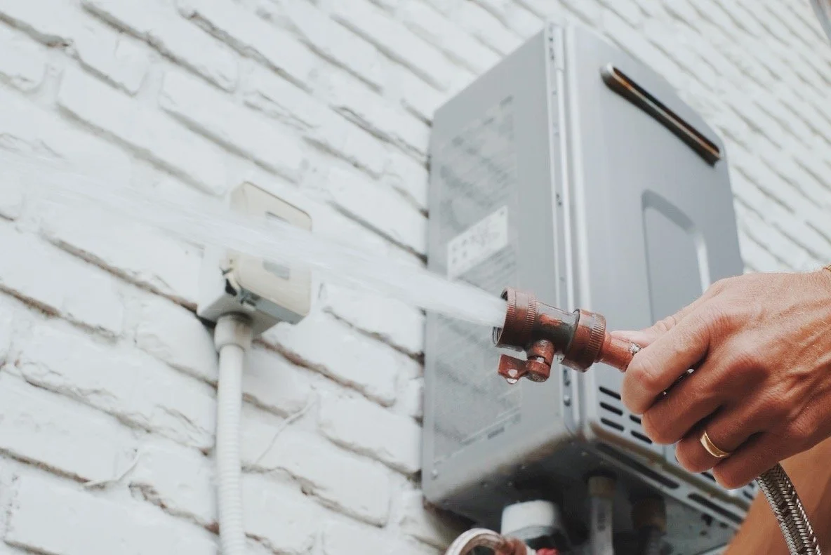 Person using a fire hydrant to spray water on an outdoor wall with an electrical box.