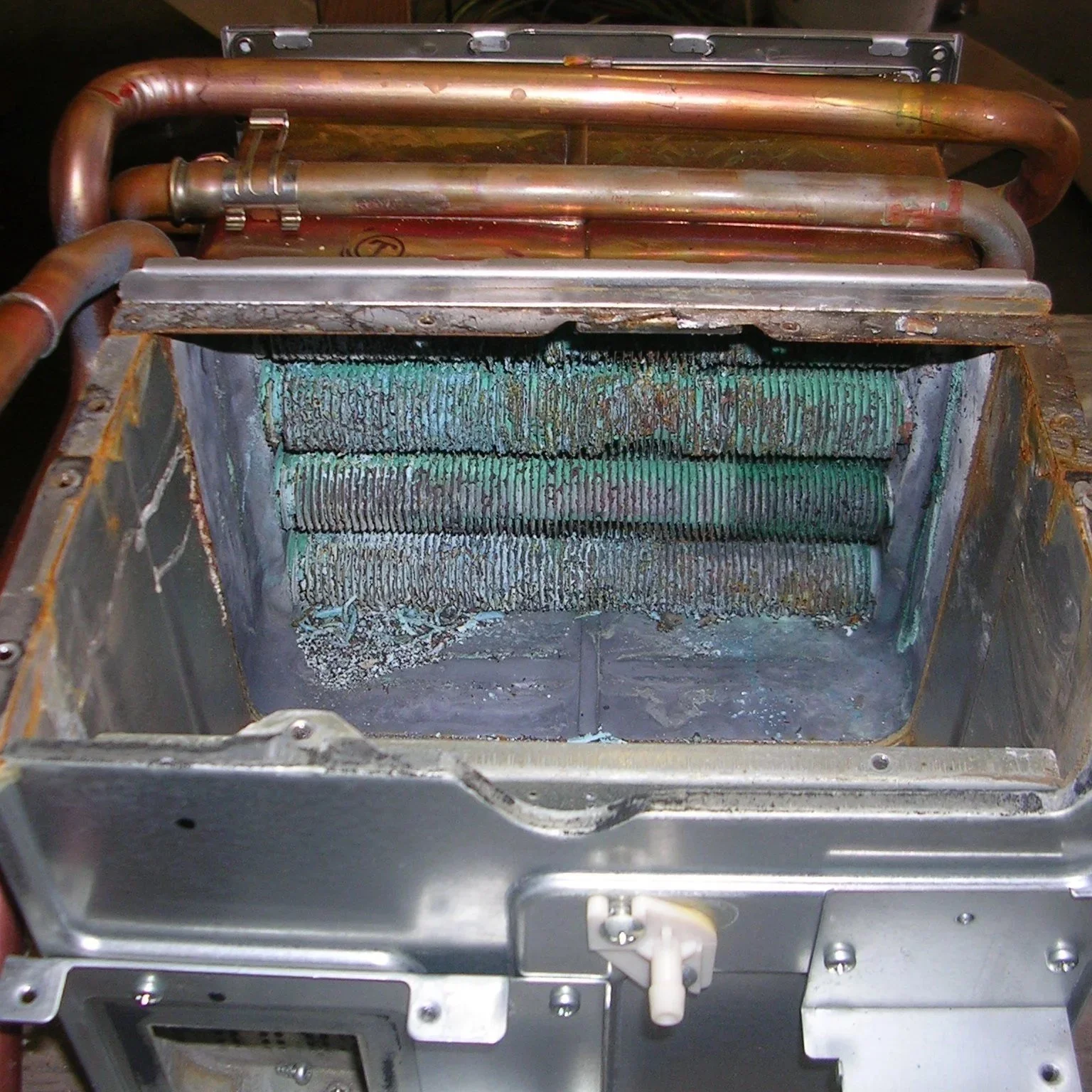 Inside view of a dirty, rusty refrigeration or air conditioning coil with corroded fins and some copper pipes.