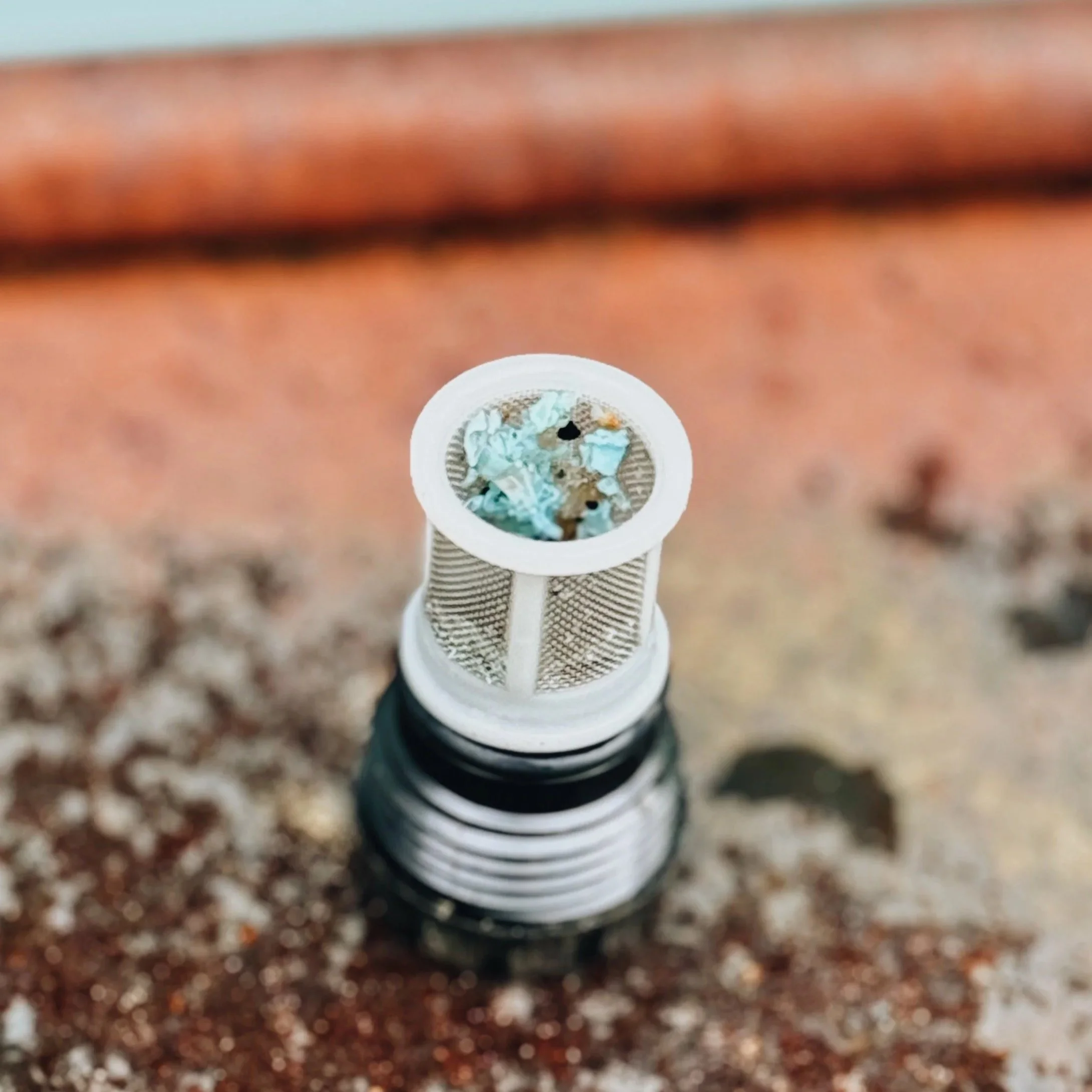“Rinnai tankless water heater filter containing green and white mineral sediment from hard water.”