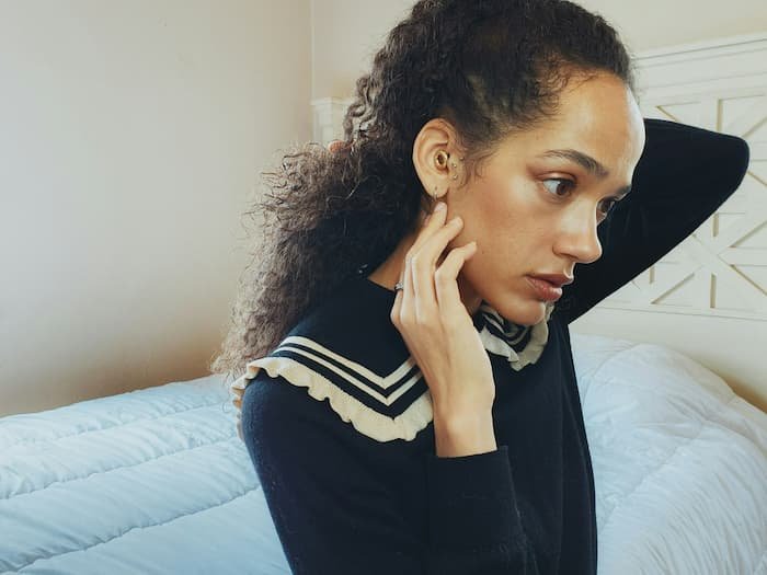 BIPOC woman rubbing her neck while sitting in her bedroom