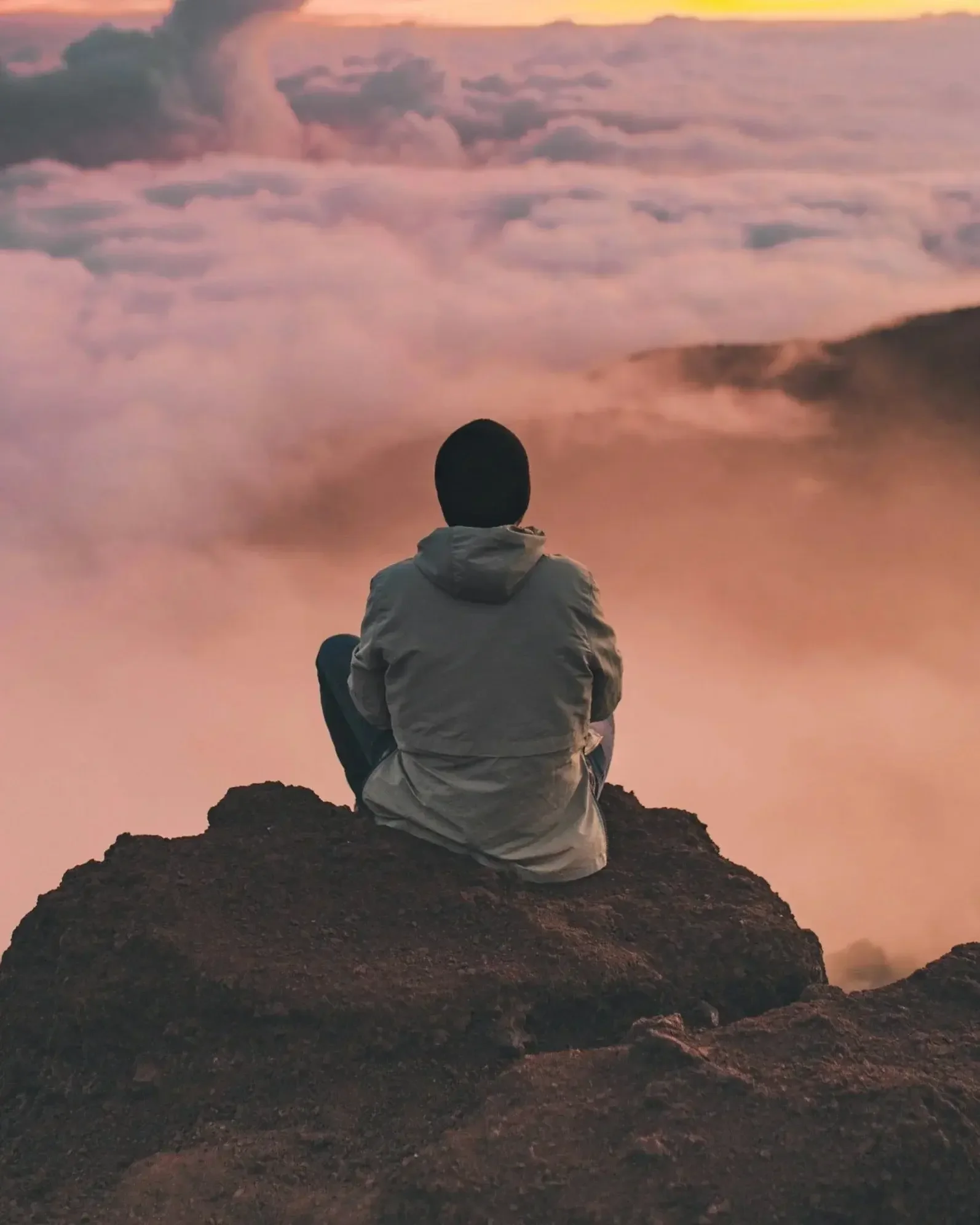 man sitting on cliff edge overlooking the clouds