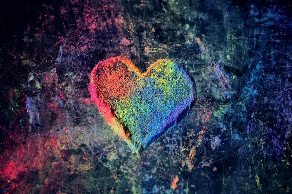 Colorful rainbow heart drawn on dark textured surface with chalk or powder.