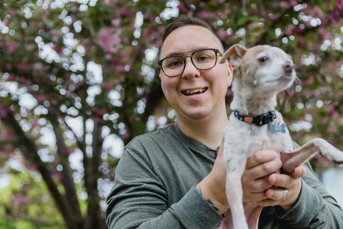 man or gender expansive person holding a dog outside