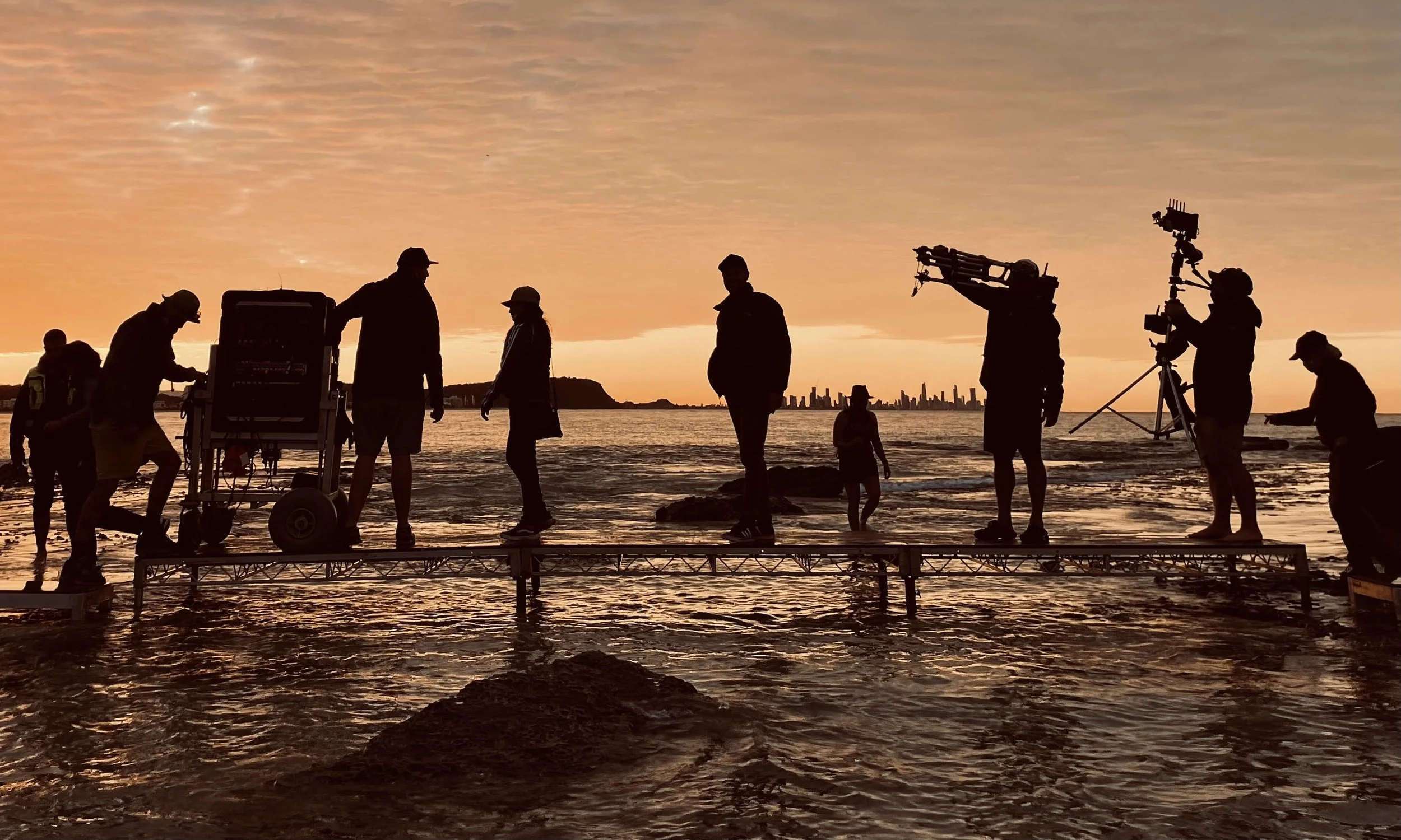 Film crew silhouetted against a golden sunset during an outdoor location shoot