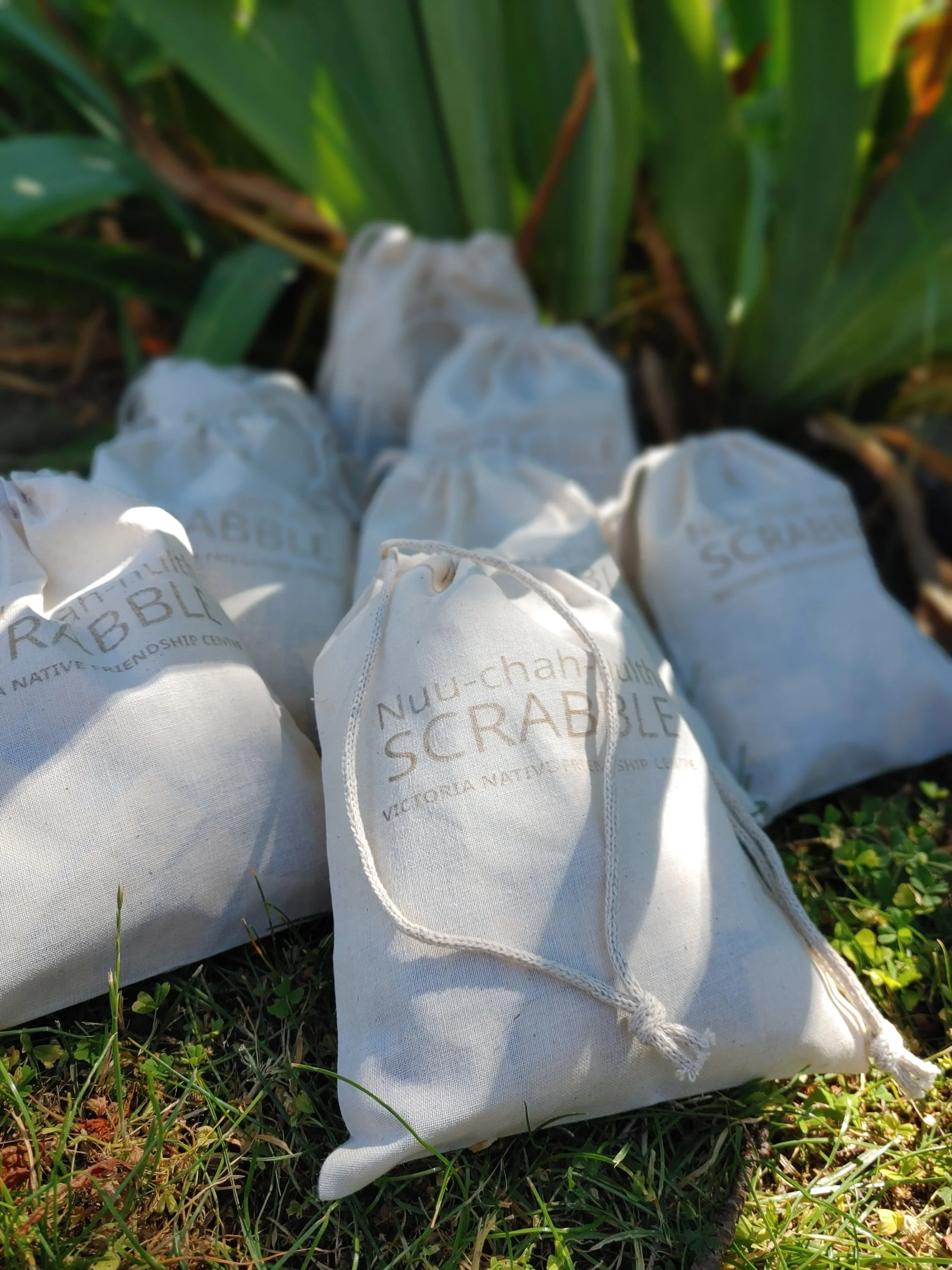 Drawstring bags labeled 'Nuu-chah-nulth Scrabble' on grass