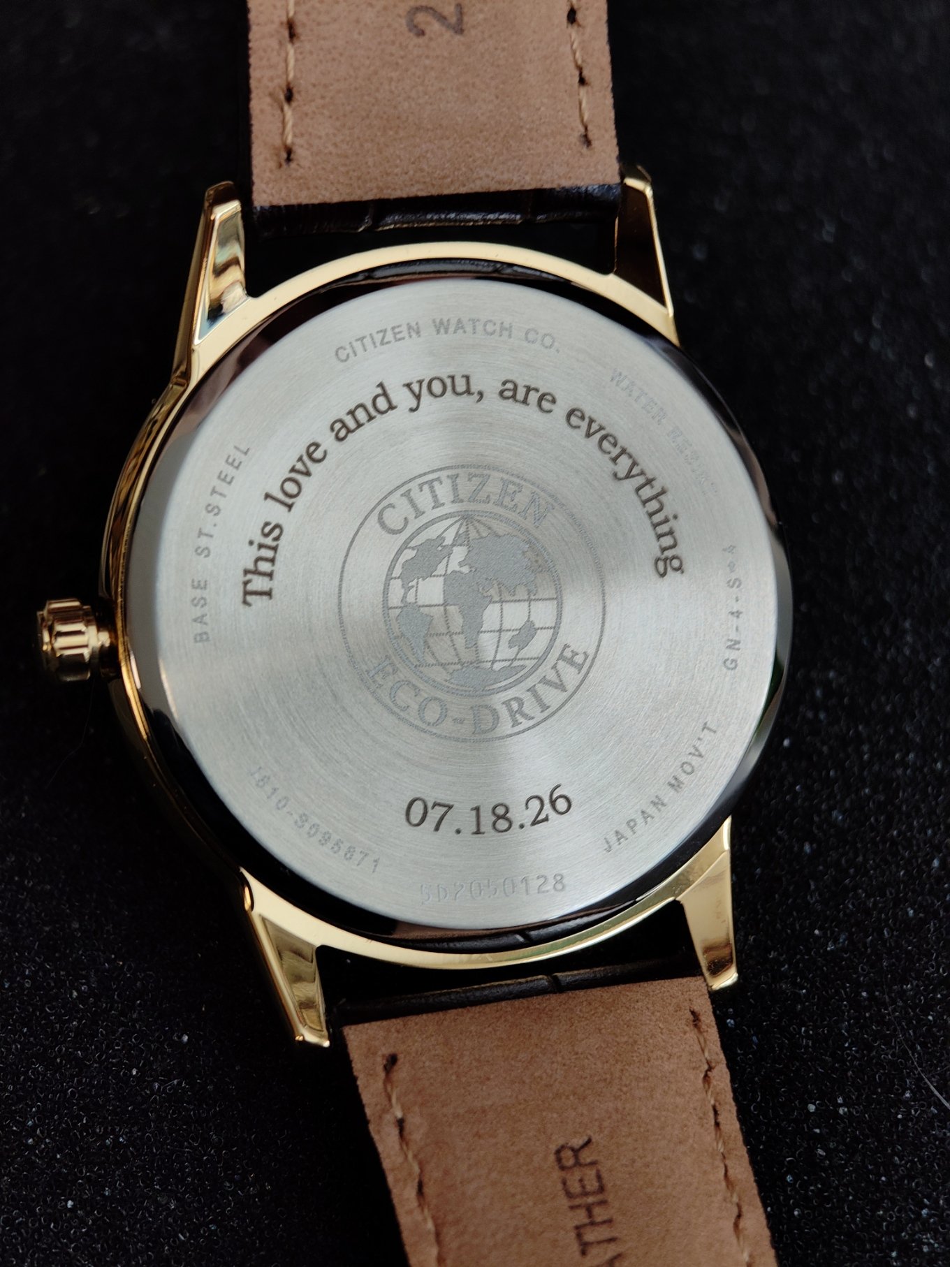 Back of a wristwatch with laser engraving message. The watch is silver Citizen Eco Drive with a brown strap.