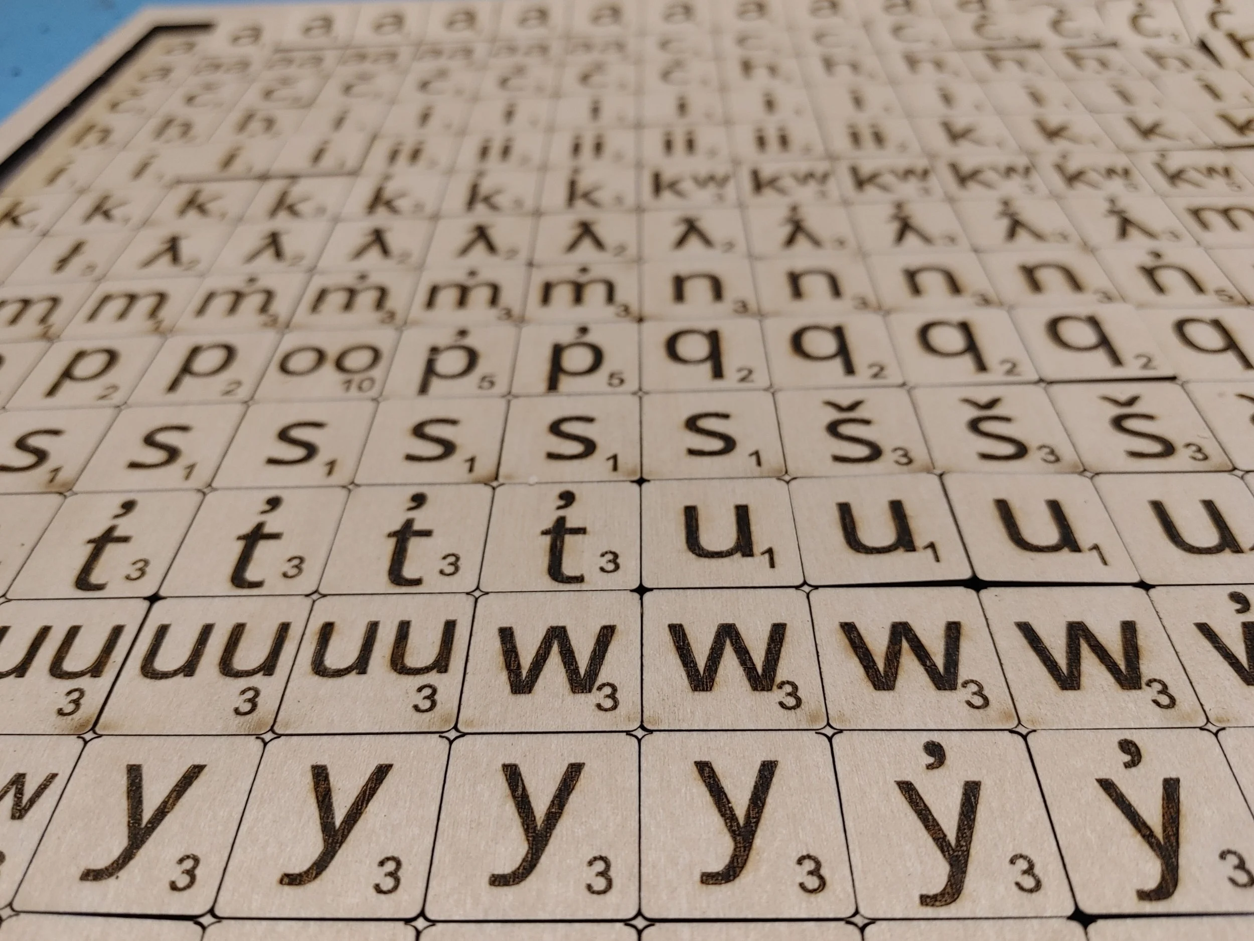Wooden Scrabble tiles with various letters and diacritical marks, each with a number indicating point value, arranged in a grid pattern.