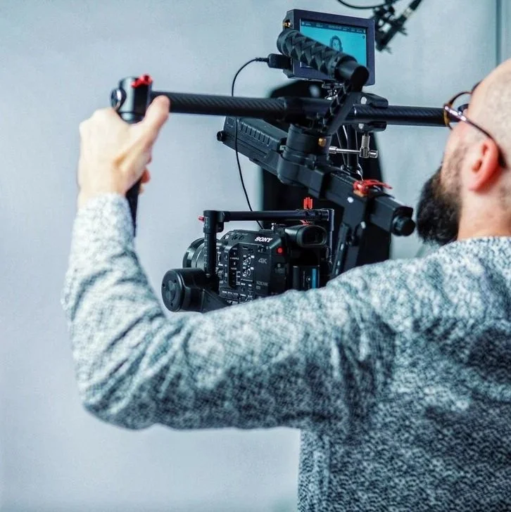 A man operating a professional video camera with a monitor attached, capturing footage indoors.