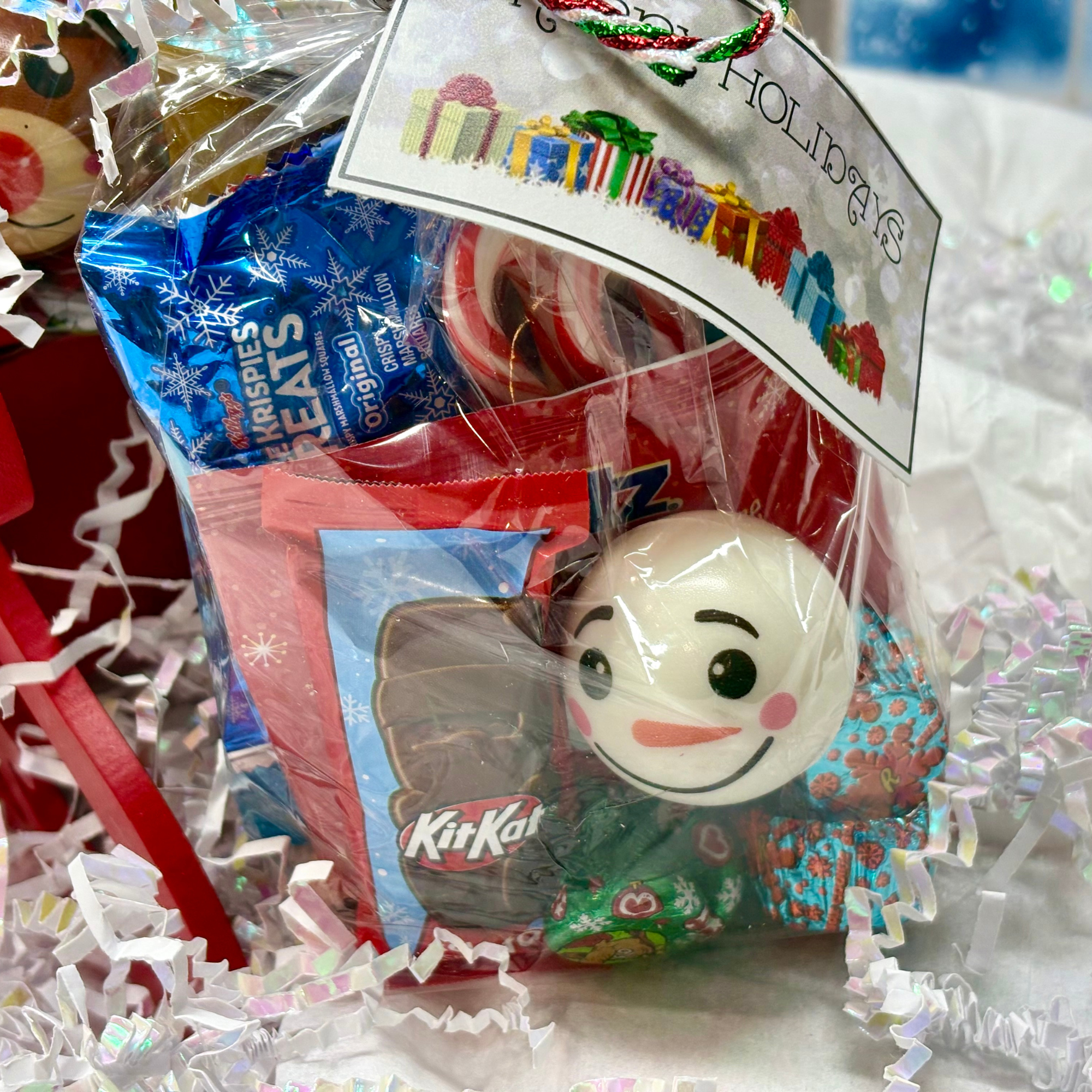 Holiday goody bag with candy, snacks, and a holiday squishy toy wrapped in clear cellophane with ribbon.