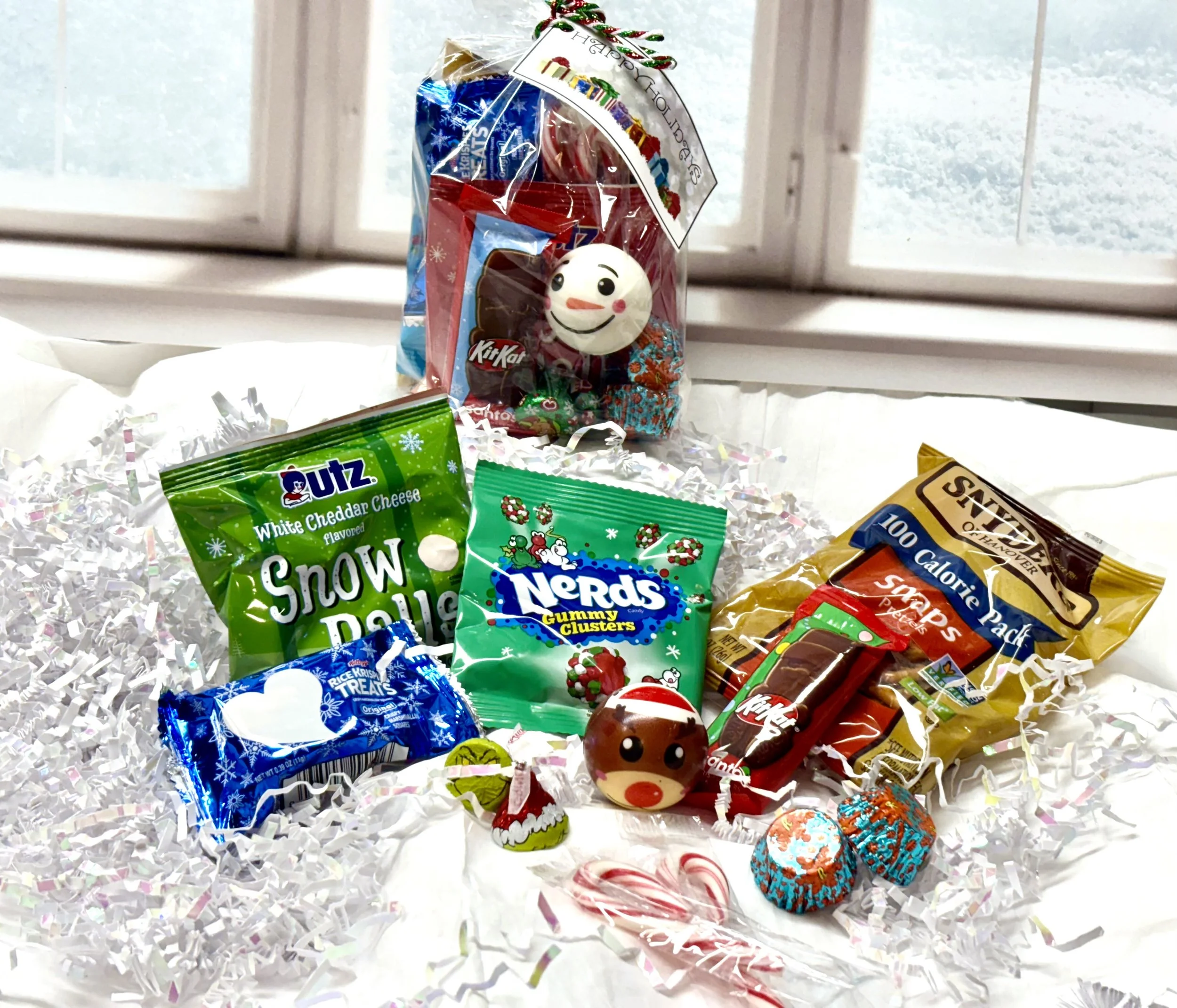 Holiday treat bag contents including Snow Balls, Nerds Gummy Clusters, Rice Krispie Treat, pretzels, chocolates, and squishy toy.