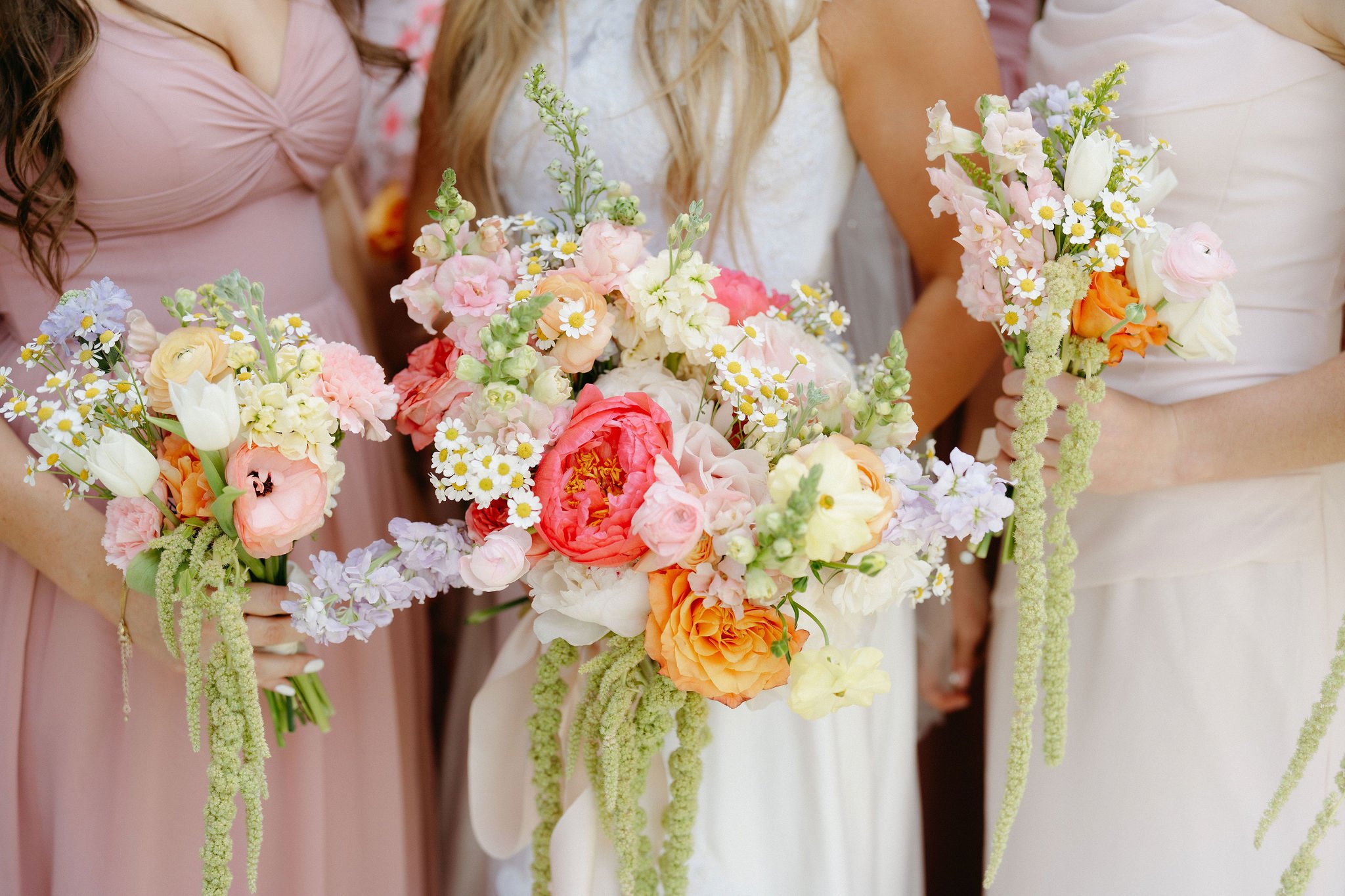 Close-up of women holding colorful flower bouquets at a celebration, wearing pastel dresses.