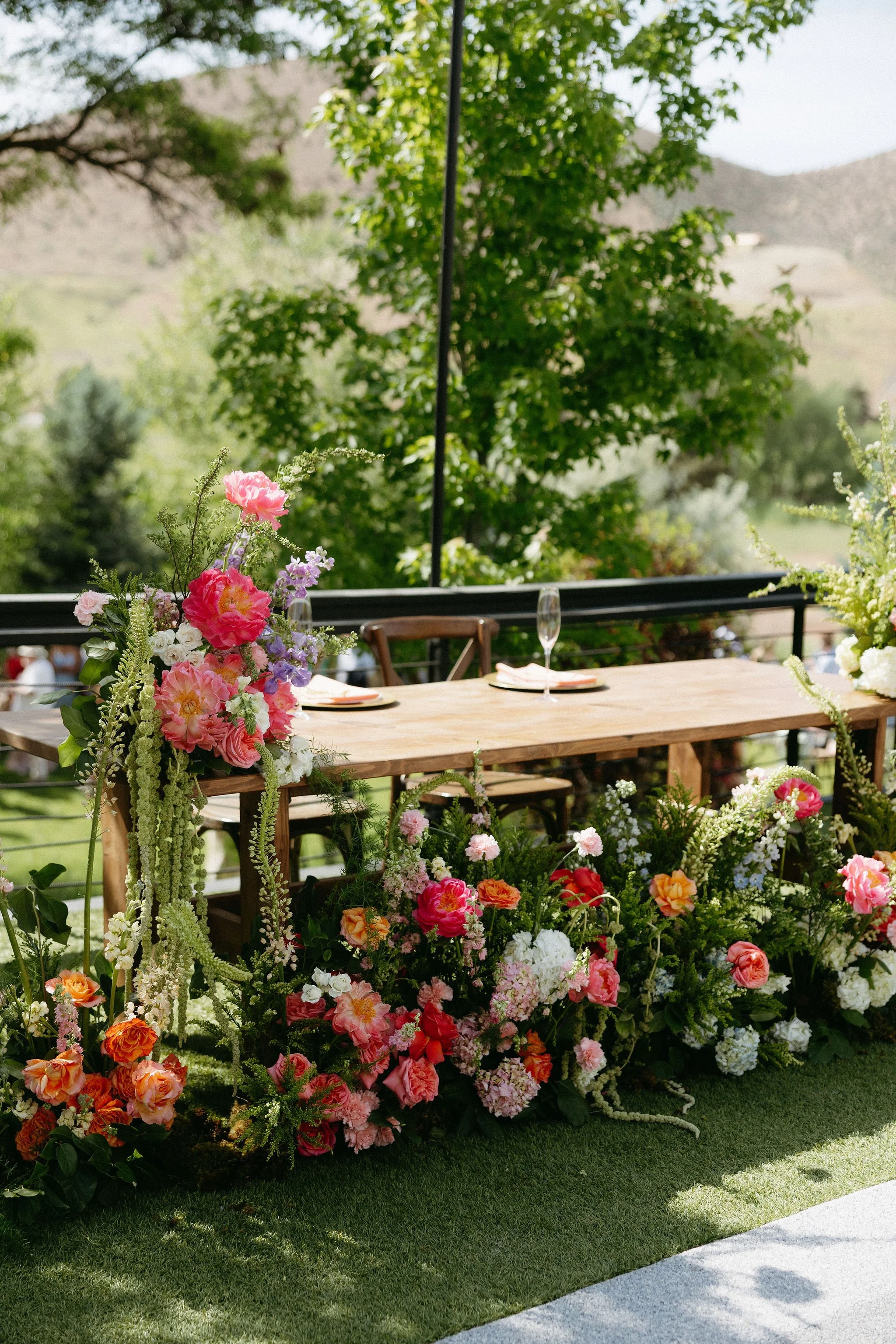 A table with floral arrangements and place settings outdoors with a mountainous landscape in the background.