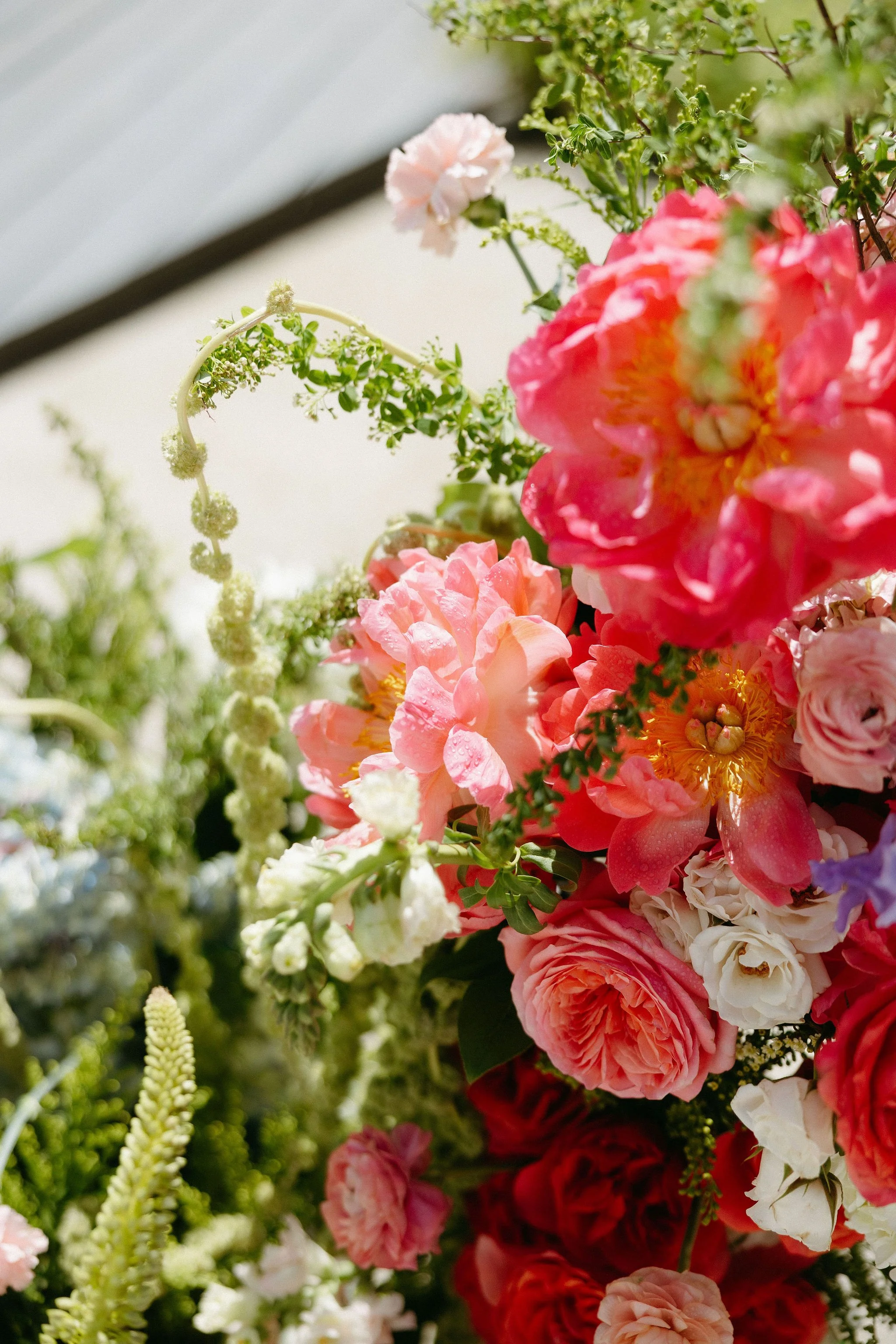 A colorful arrangement of various flowers including pink, red, white, and purple blooms, with some greenery and small white blossoms.