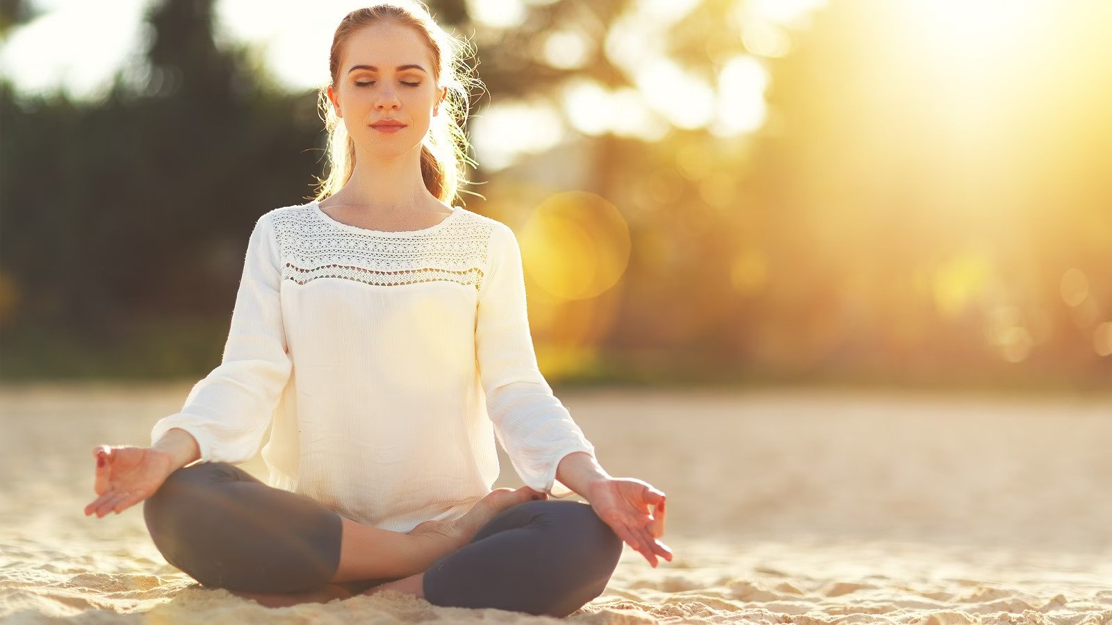 Woman meditating on a beach at sunset