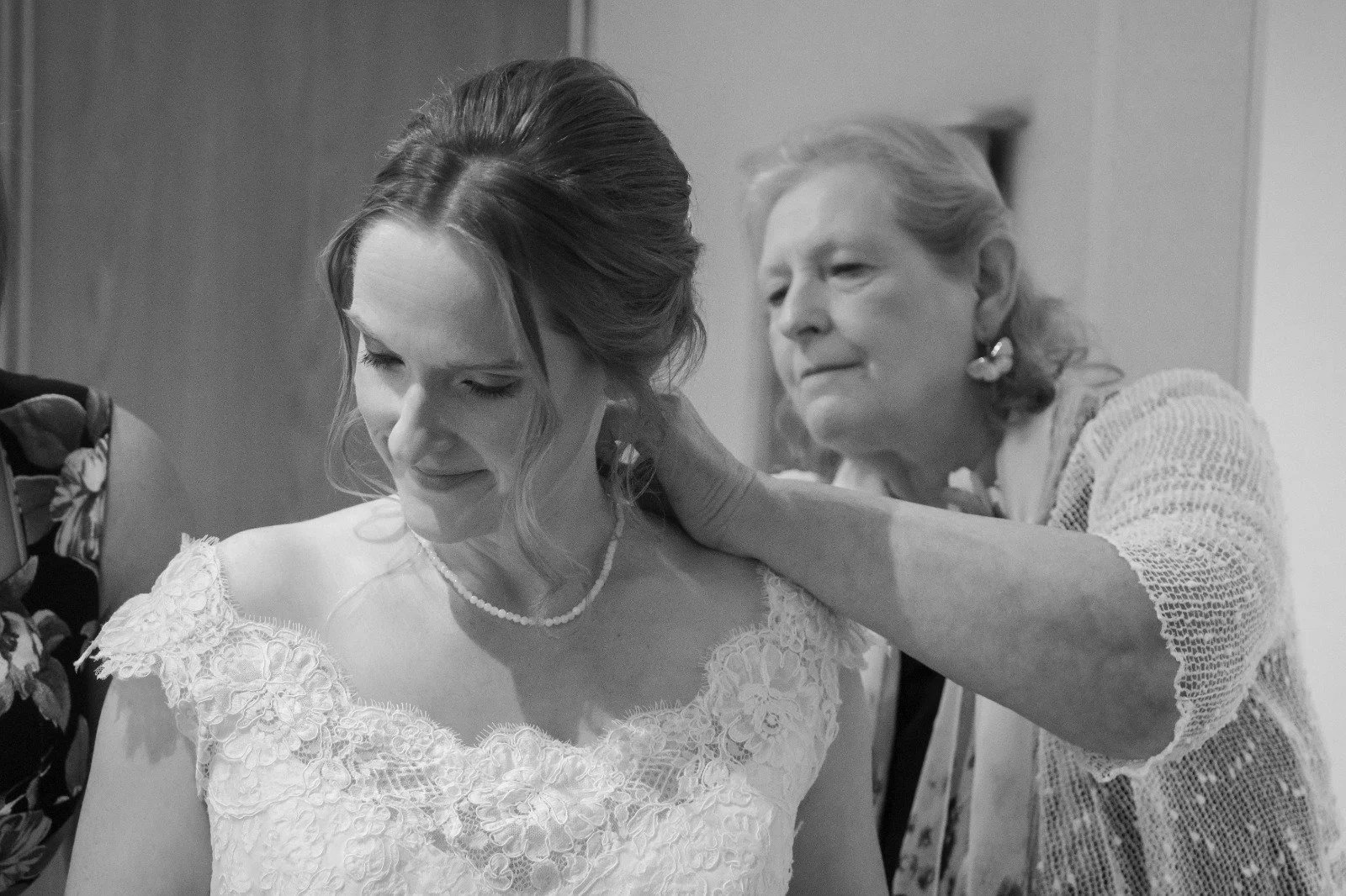 An older woman helping a young woman adjust her wedding dress in a dressing room.