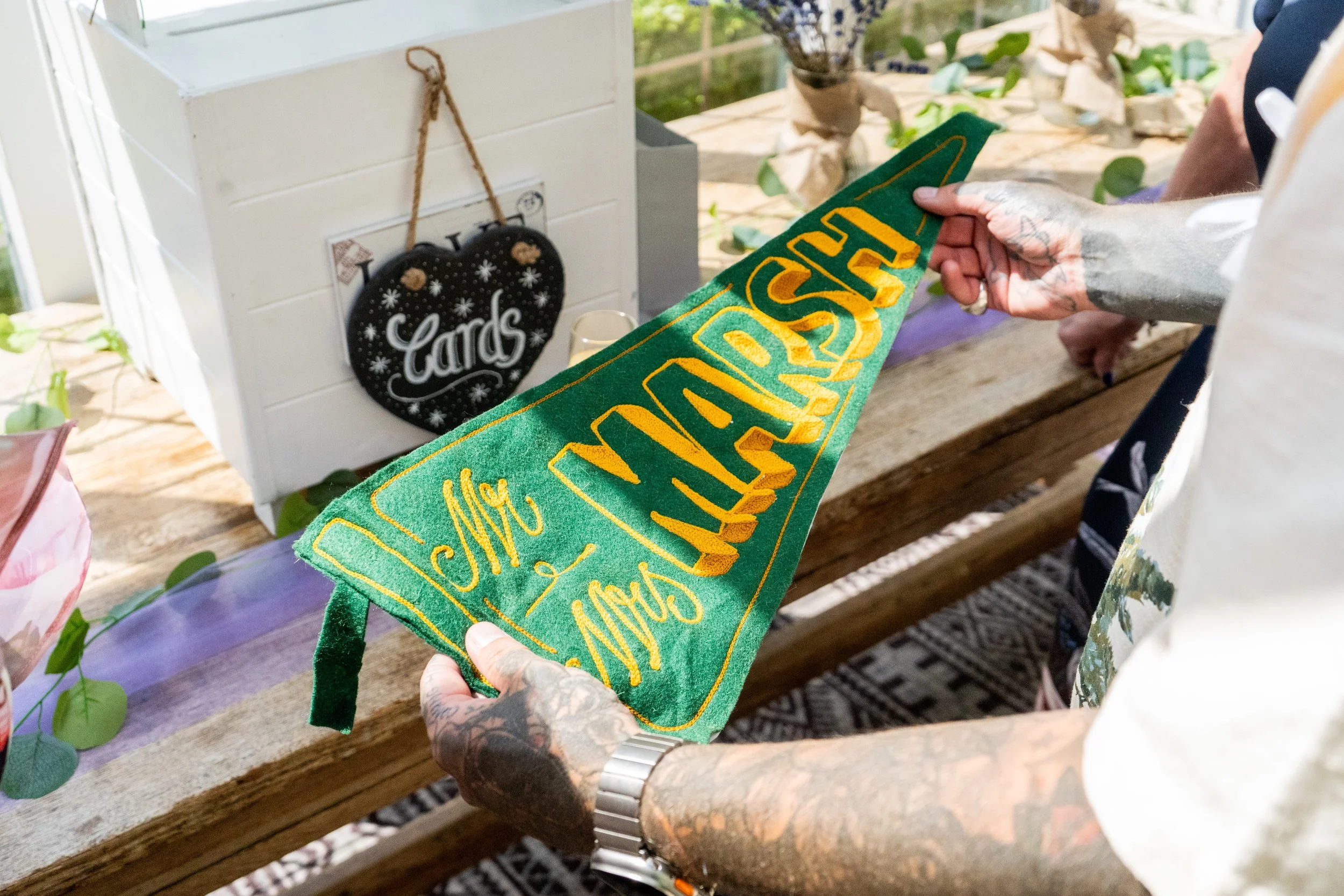 Person holding a green felt Christmas stocking with yellow embroidery that reads 'Merry Christmas' in a cozy, decorated space with a white card box and black pillow with the word 'Cards' in the background.