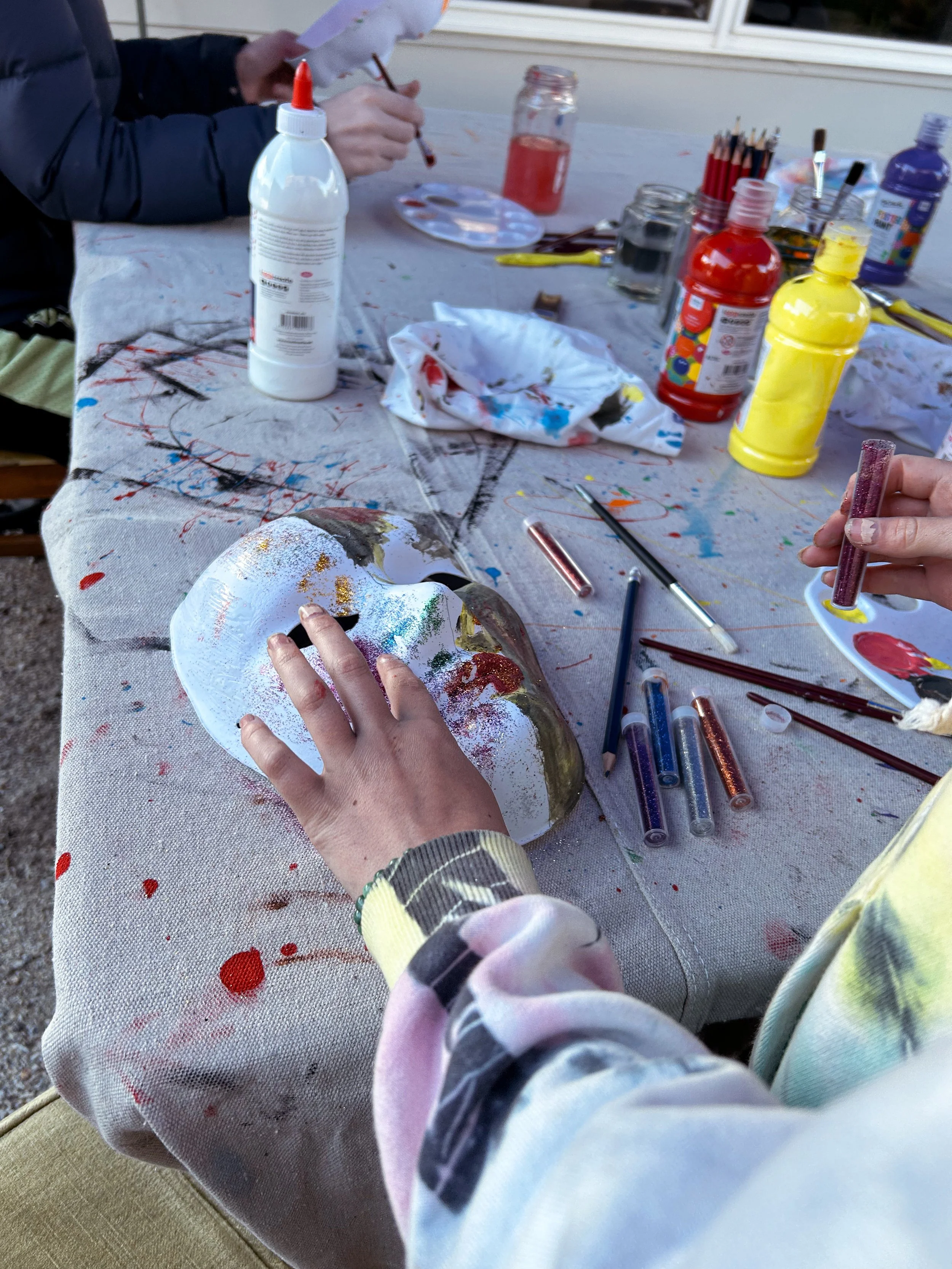 People painting and decorating a white skull sculpture at an outdoor arts and crafts table.